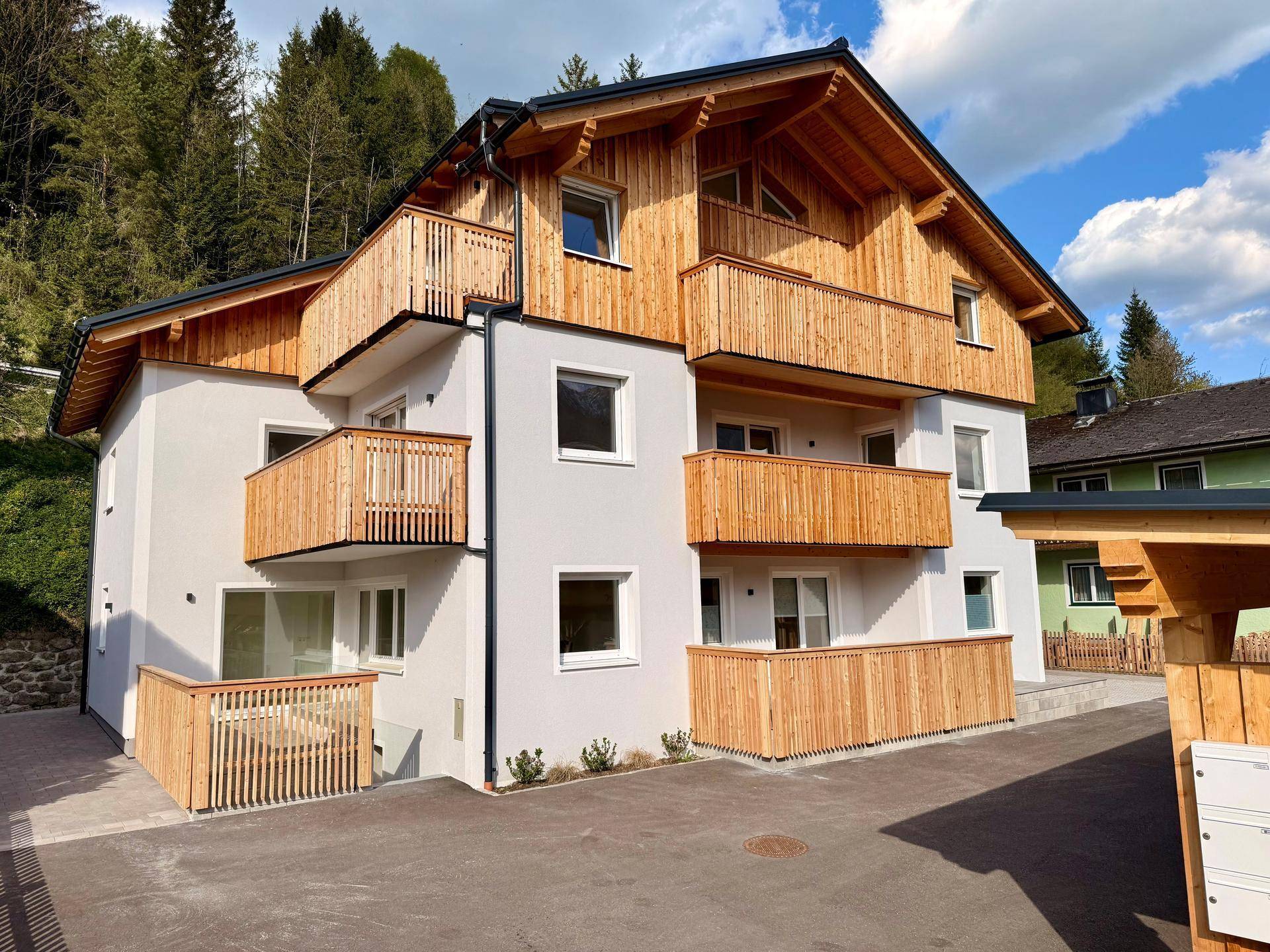 Attraktives Mehrfamilienhaus mit weißer Fassade und mehreren Holz-Balkonen in grüner Umgebung.