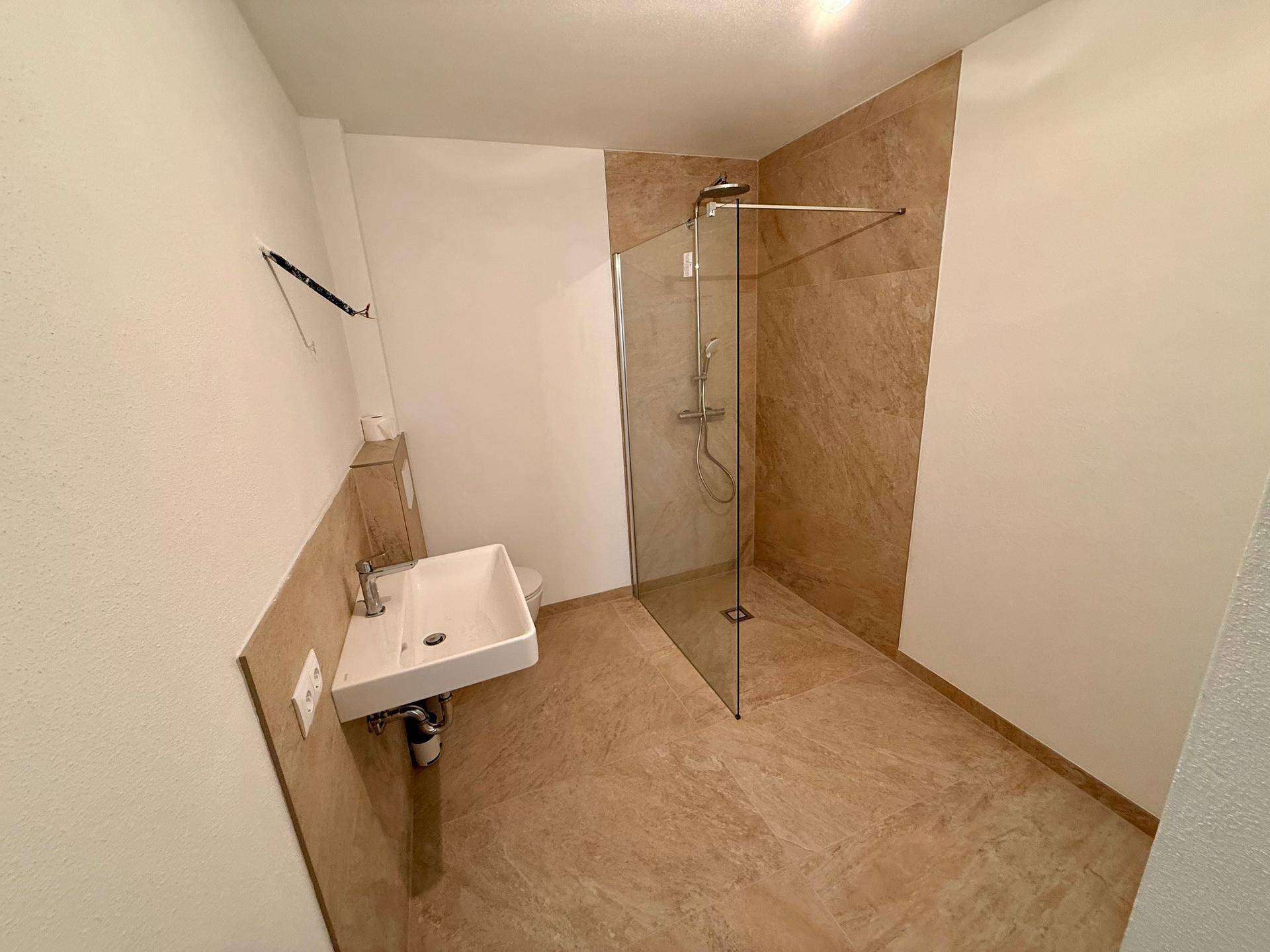Modernes Badezimmer mit begehbarer Dusche, Waschbecken und beigefarbenen Fliesen.