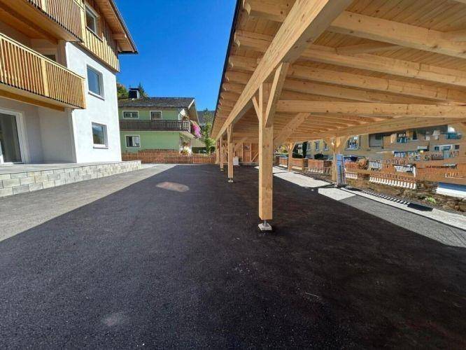 Langer Holz-Carport mit mehreren Stellplätzen auf einem asphaltierten Parkplatz.