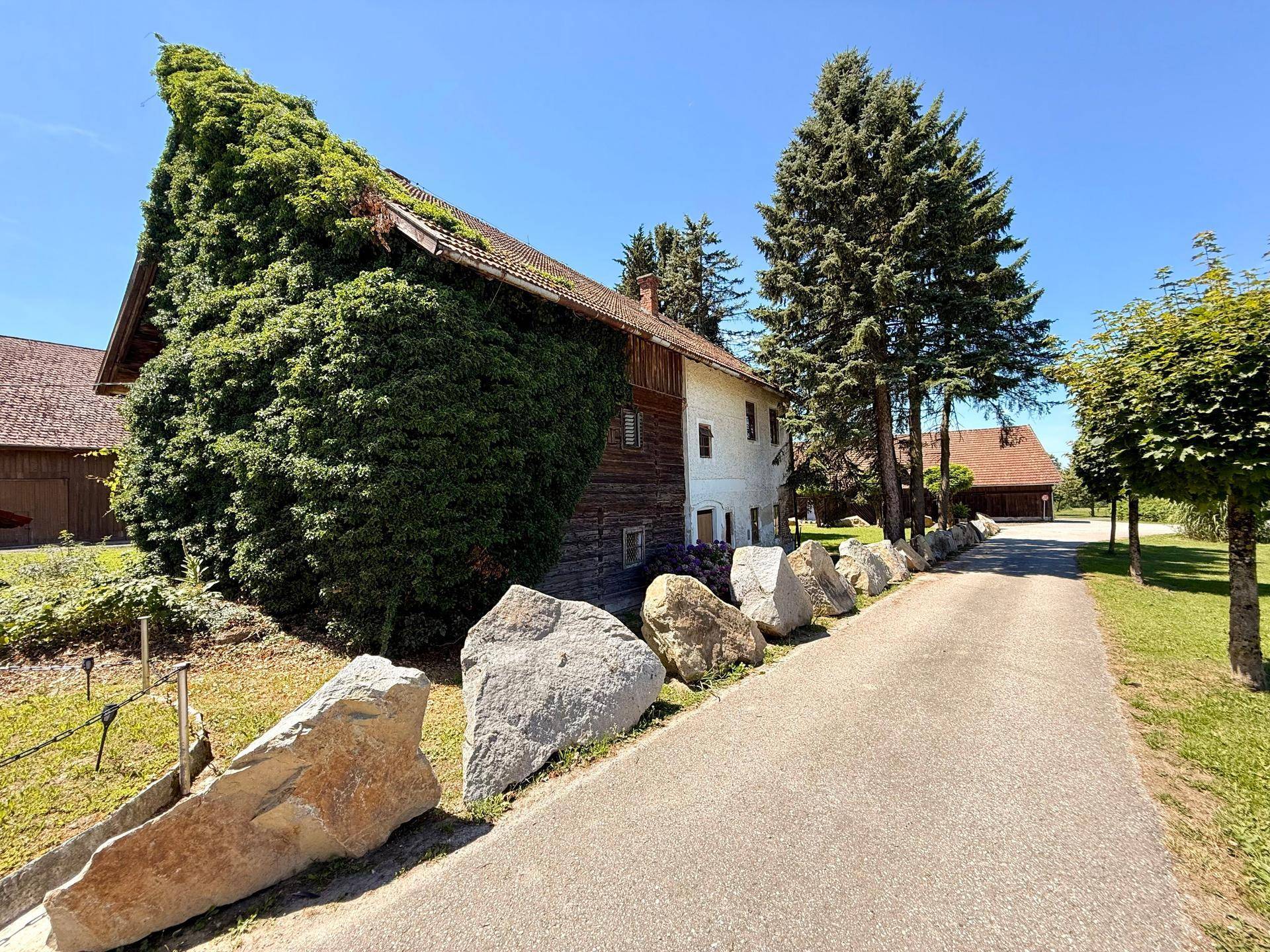 Traditionelles Gebäude, teilweise mit Efeu bewachsen, an einer von großen Steinen gesäumten Auffahrt.