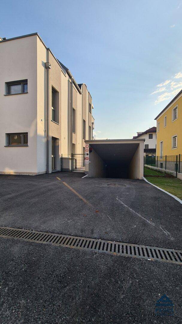 Zufahrt zur Tiefgarage einer modernen Wohnanlage mit heller Fassade bei Sonnenlicht.
