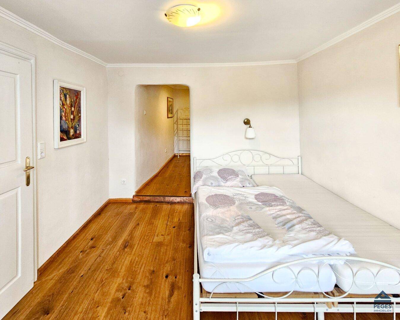 Geräumiges Schlafzimmer mit Holzboden und einem Durchgang zu einem weiteren Bereich.
