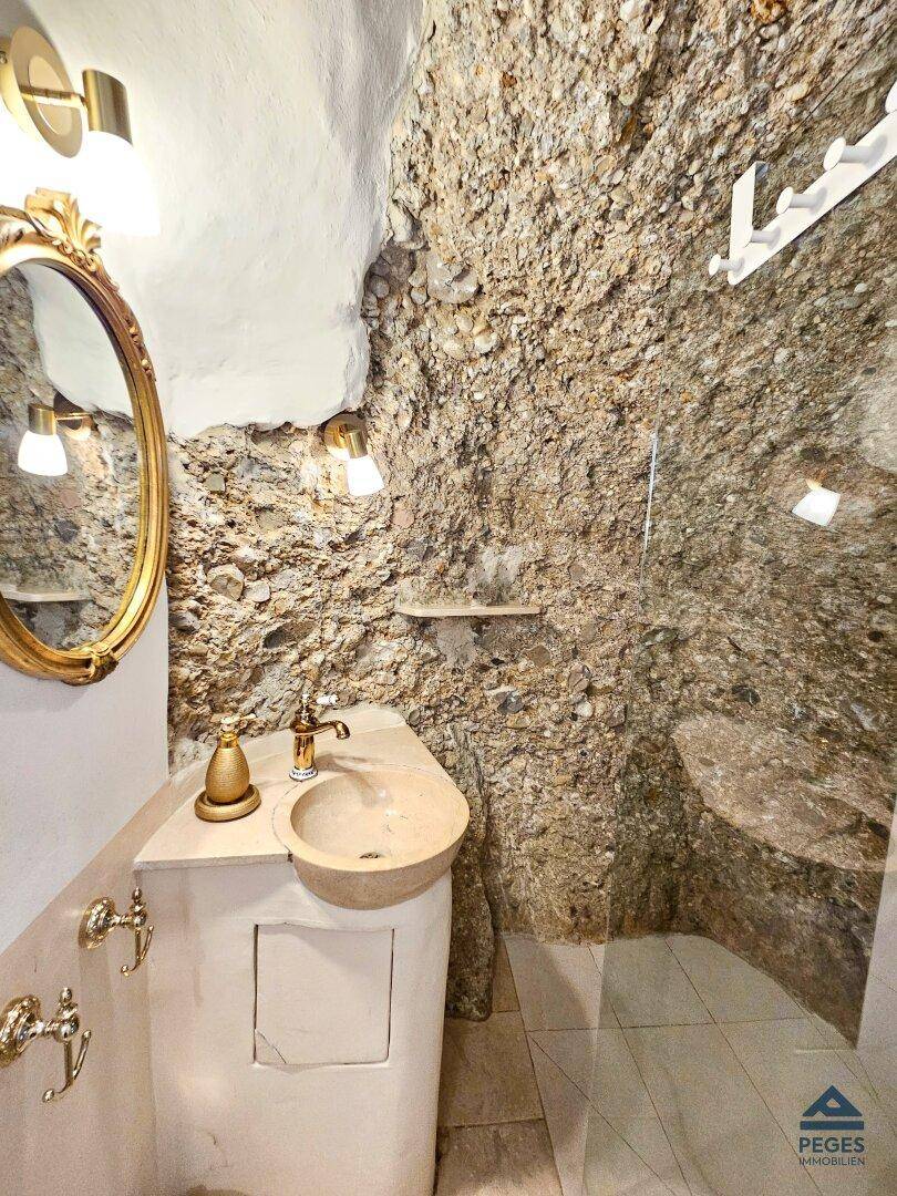 Einzigartiges Badezimmer mit freiliegender Felswand, modernem Waschbecken und Duschbereich.
