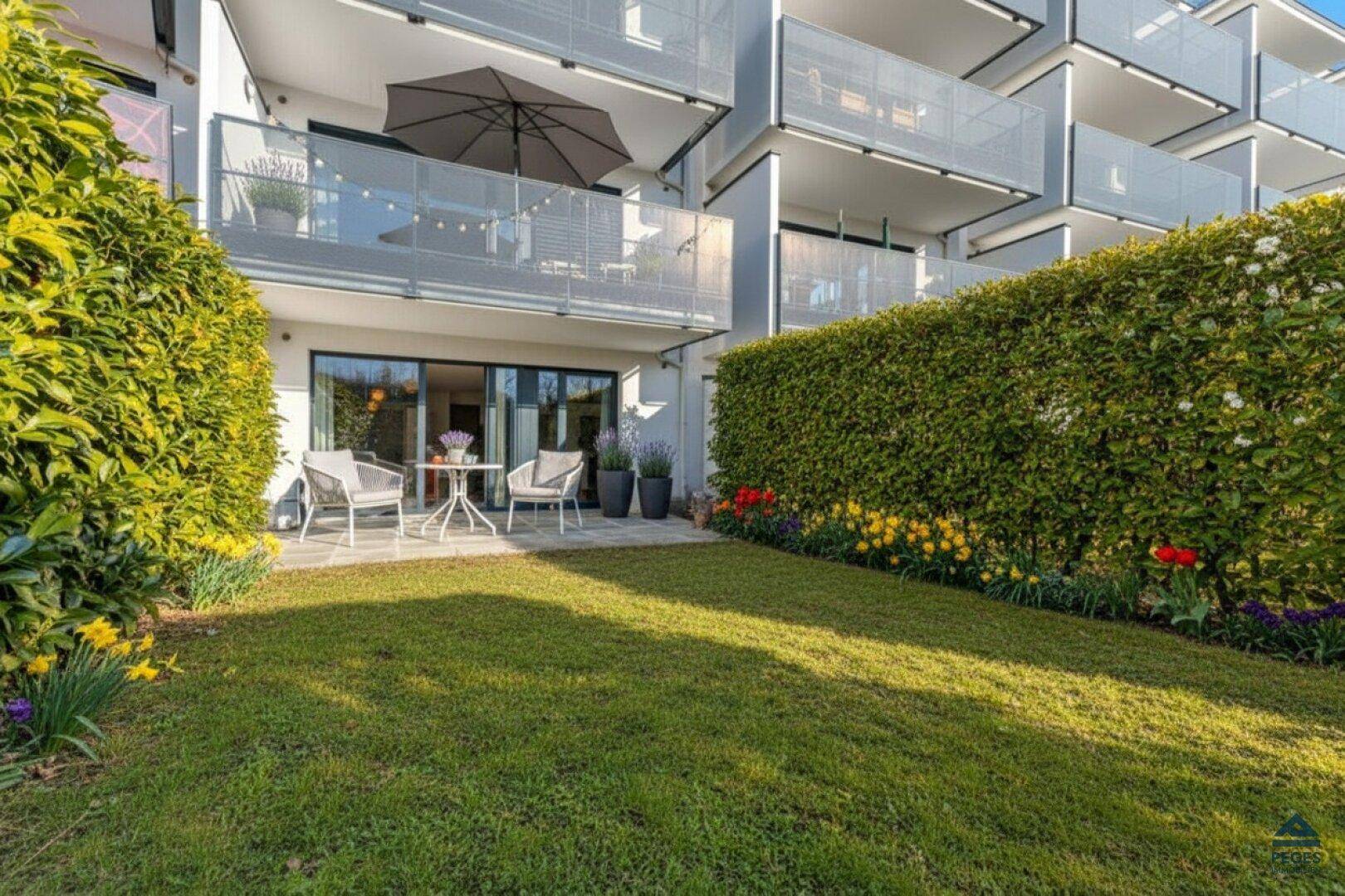 Gepflegter Gartenbereich mit Terrasse vor einem modernen Wohngebäude mit Balkonen.