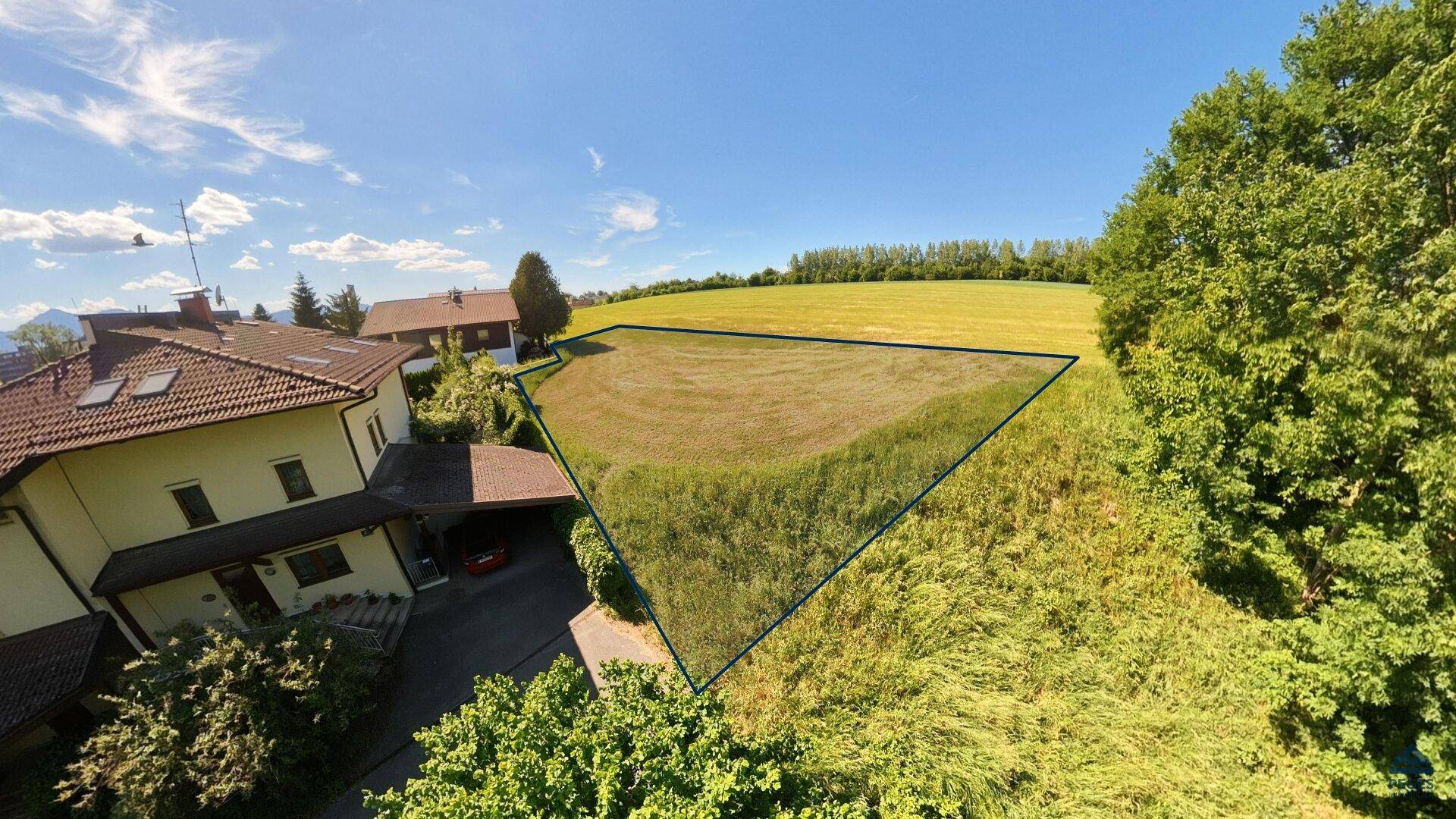 Luftaufnahme eines dreieckigen Grundstücks neben einem Wohnhaus mit Carport und grüner Umgebung.