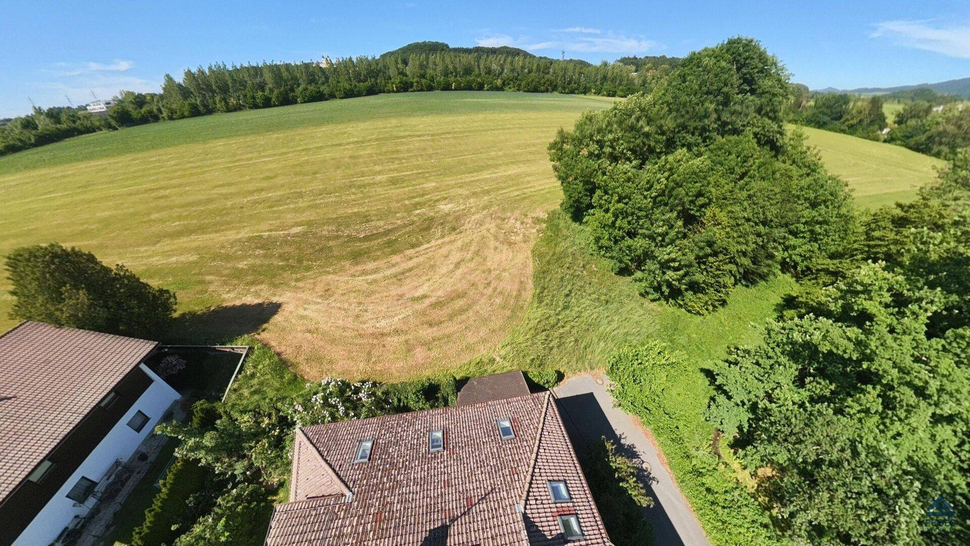 Luftaufnahme eines Hauses mit Ziegeldach, eingebettet in eine hügelige Landschaft mit grünen Feldern und Bäumen.