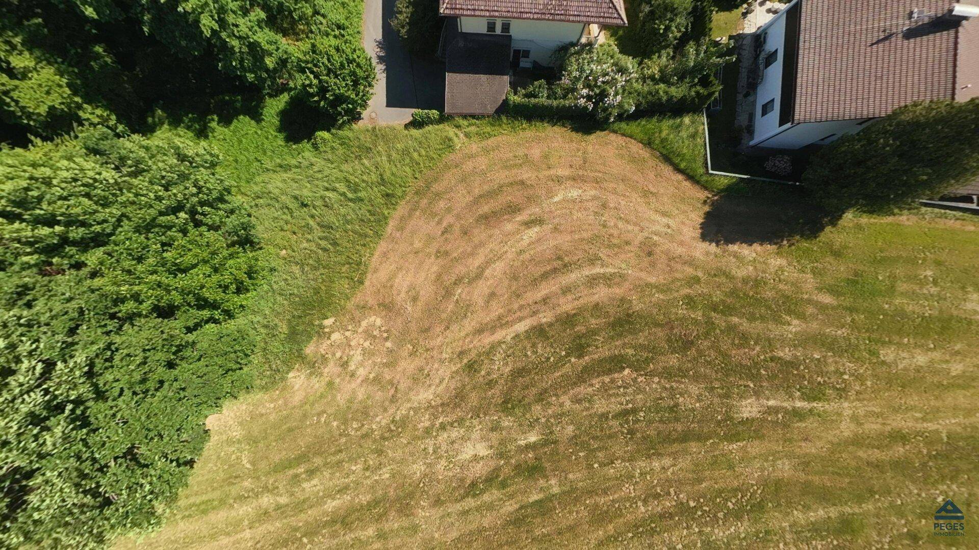 Detaillierte Luftaufnahme eines unbebauten Grundstücks mit natürlicher Vegetation und angrenzenden Häusern.