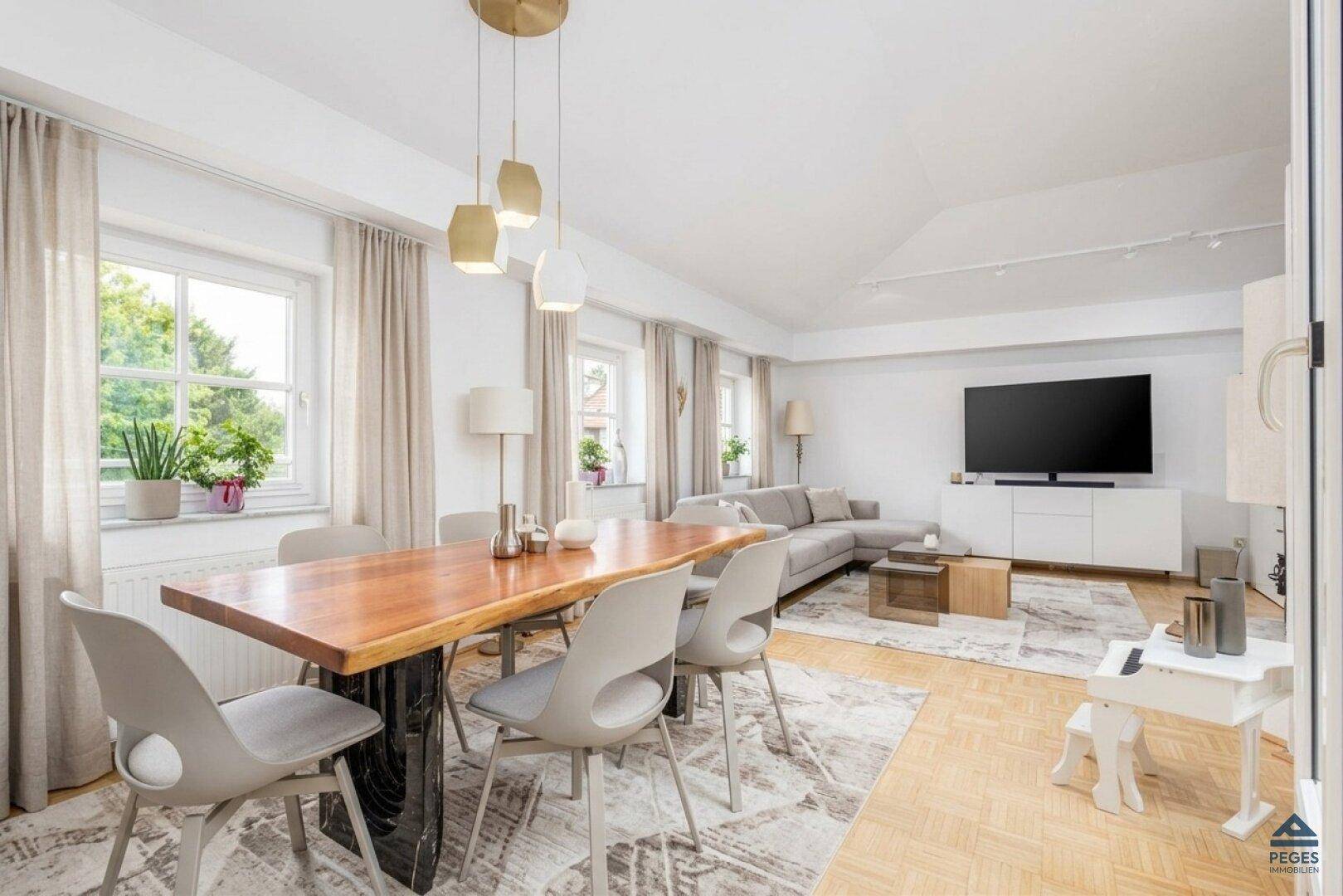 Geräumiger Wohn-Essbereich mit Holztisch, bequemer Couch und großen Fenstern für viel Licht.
