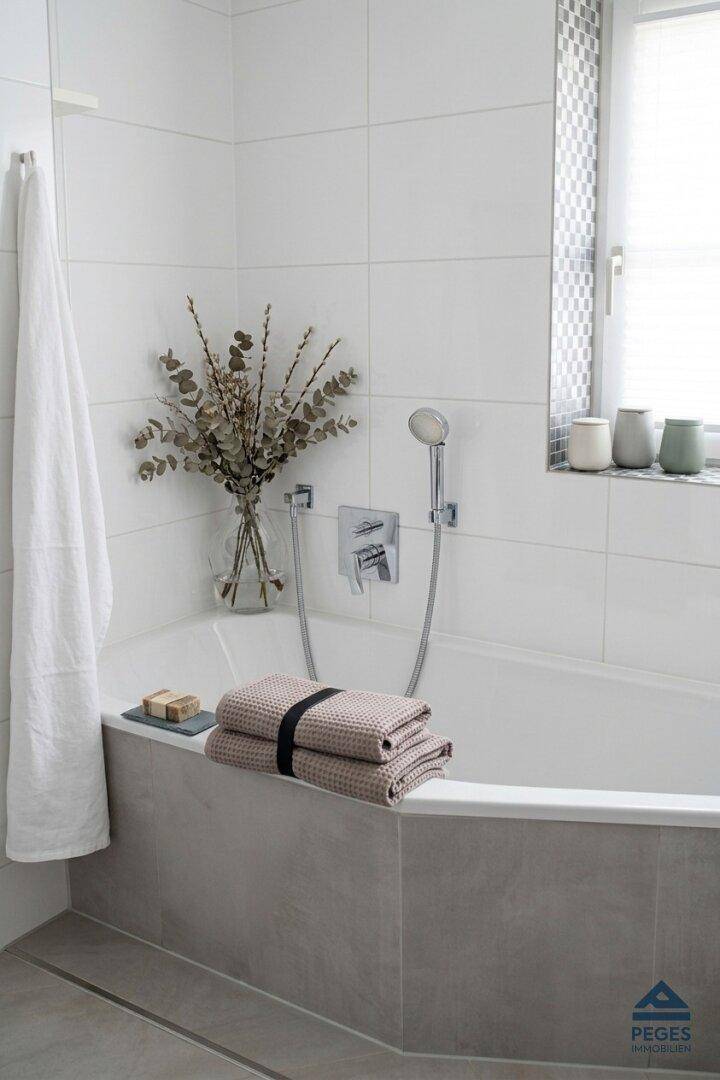 Helles Badezimmer mit Badewanne, weißen Fliesen und einem Fenster für Tageslicht.