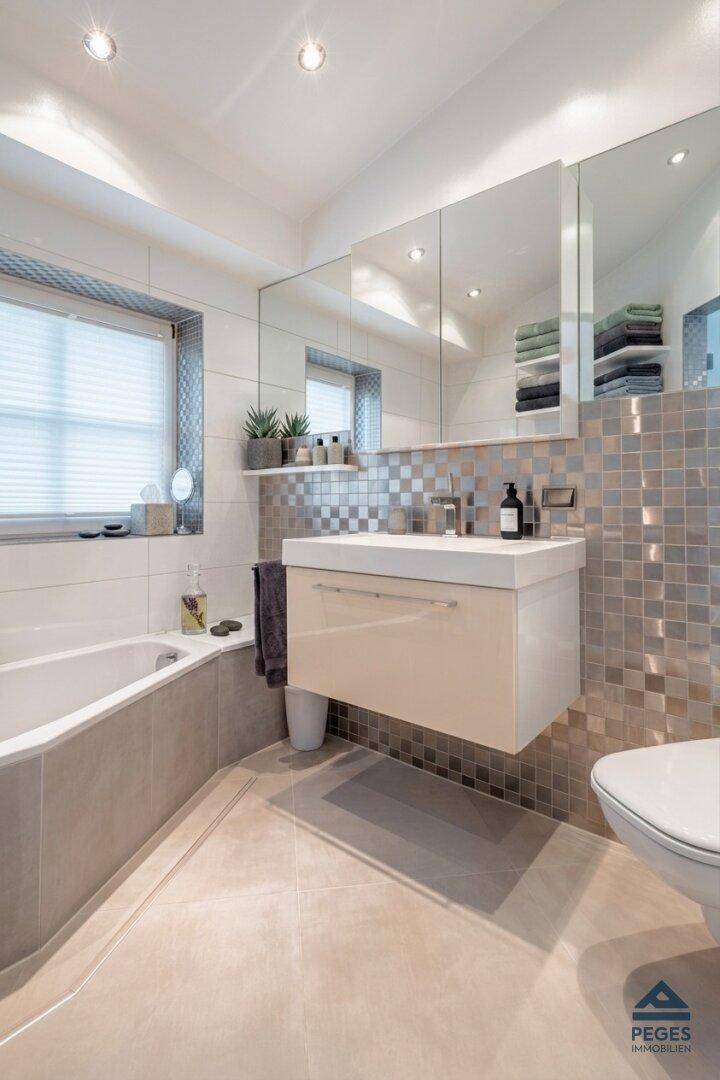 Modernes Badezimmer mit schwebendem Waschtisch, Spiegelschrank und Badewanne.