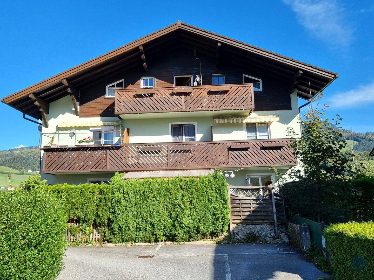 Mehrstöckiges Gebäude mit mehreren Balkonen und einer gepflegten Hecke im Vordergrund.
