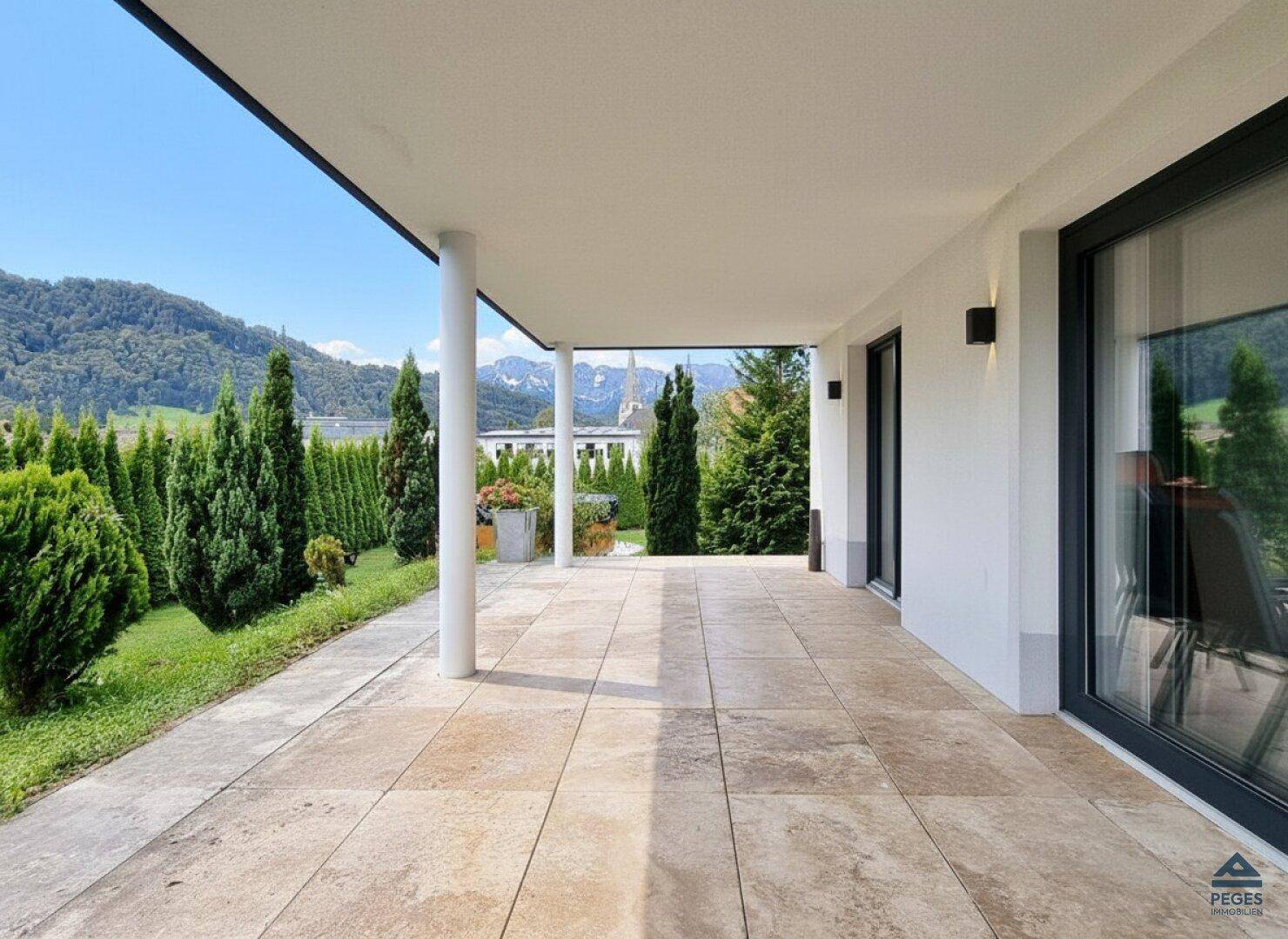 Überdachte Terrasse mit Fliesenboden und weitem Blick auf die grüne Landschaft und Berge.