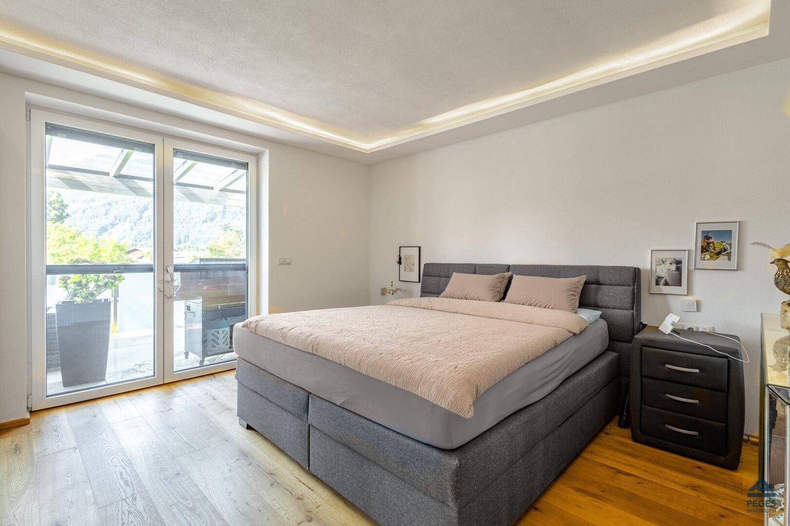 Helles Schlafzimmer mit großem Bett, Holzboden und Zugang zu einem Außenbereich mit Bergblick.
