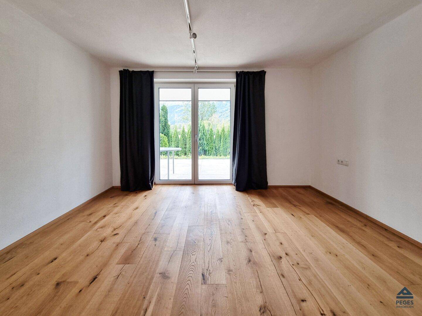Heller Wohnraum mit Holzboden und großen Fenstertüren, die viel Tageslicht hereinlassen.