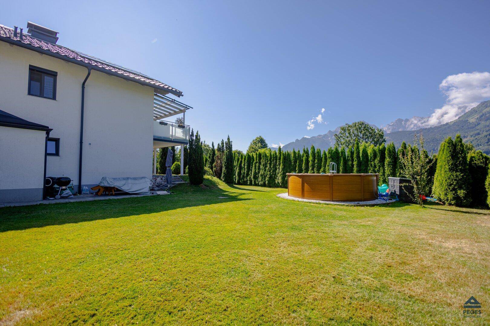 Großer gepflegter Garten mit Rasenfläche, oberirdischem Pool und Blick auf die Berge.