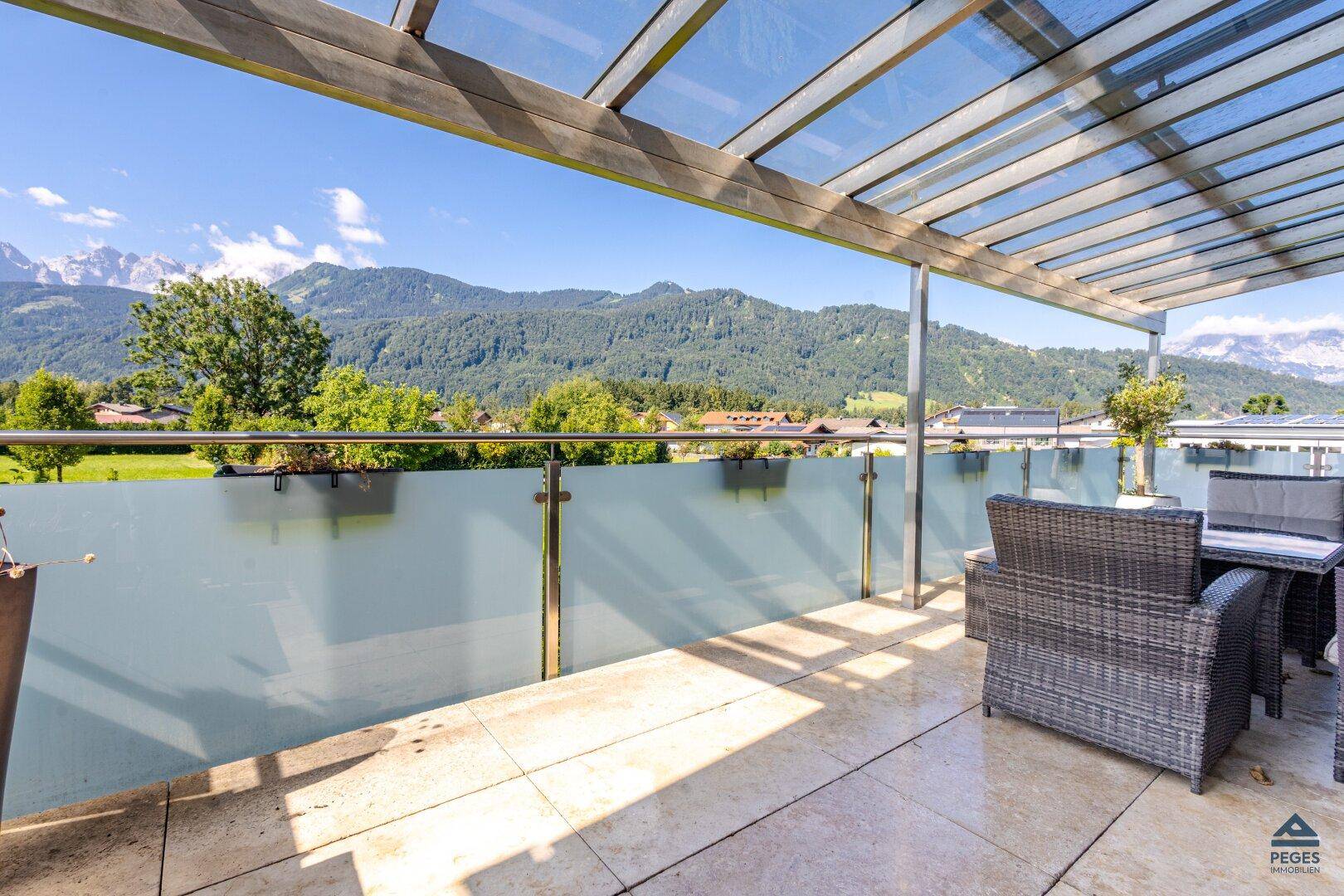 Sonniger Terrassenbereich mit Glasgeländer und weitem Blick auf die umliegende Berglandschaft.