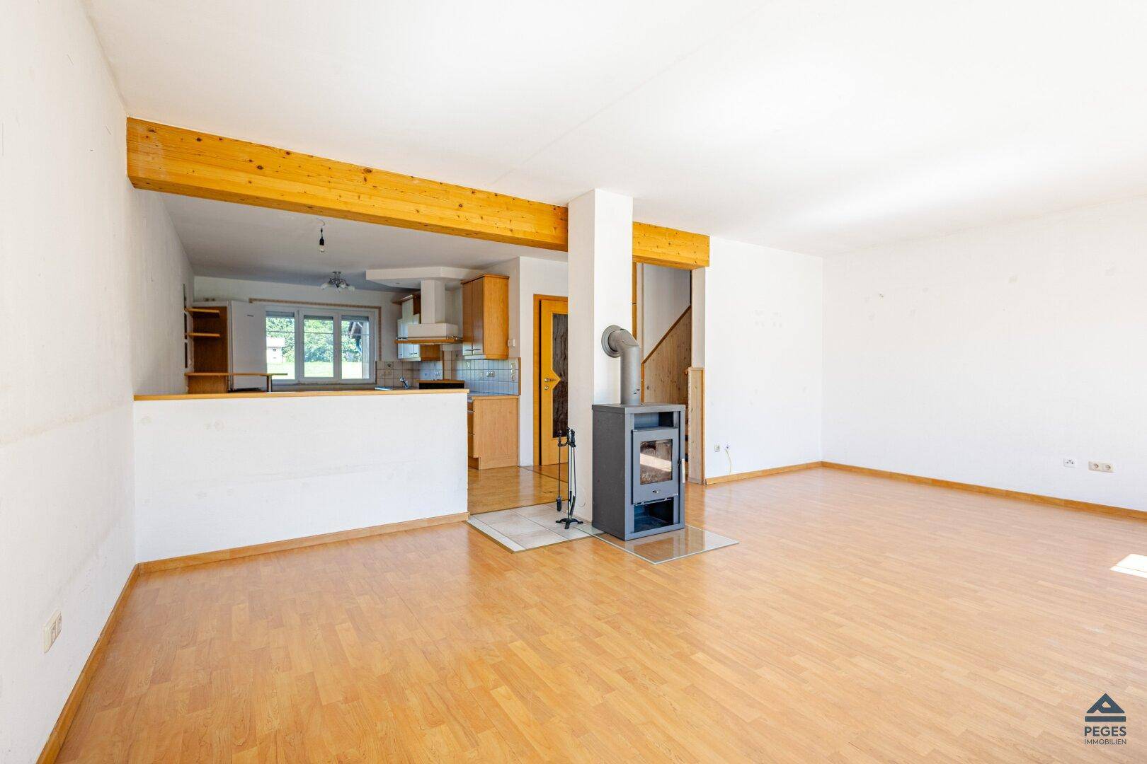 Offener Wohnbereich mit Holzboden, Kaminofen und sichtbarem Holzbalken.
