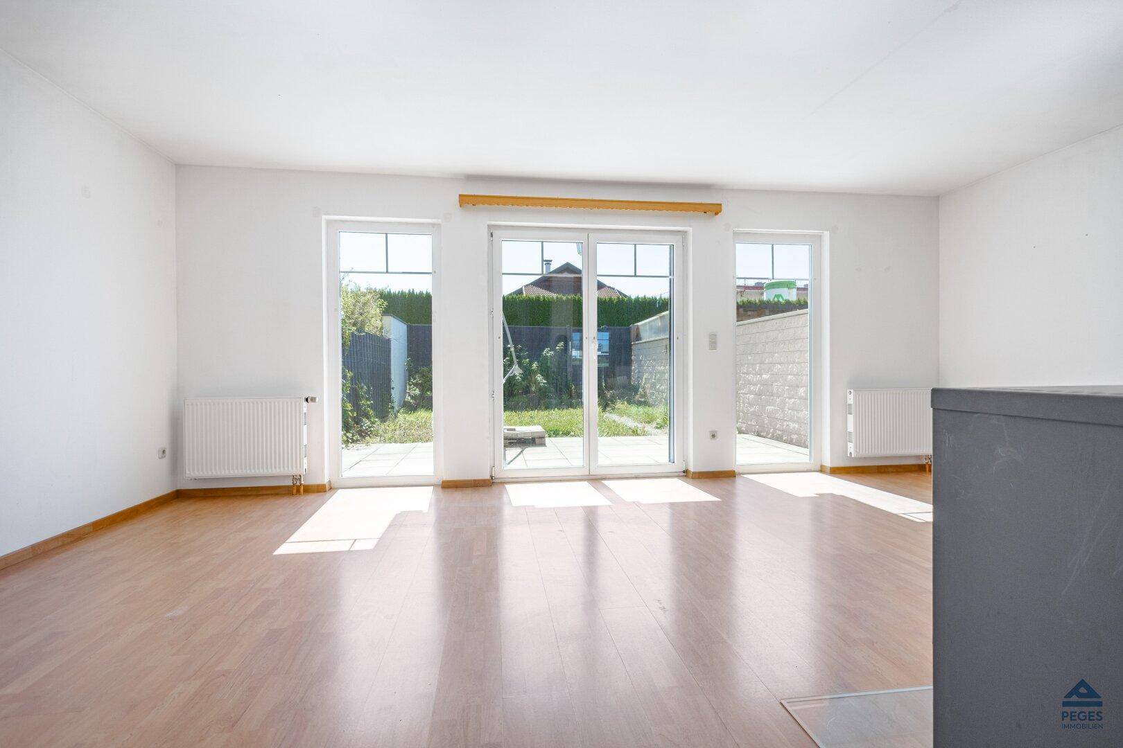 Heller Wohnraum mit großen Fenstertüren, Holzboden und direktem Zugang zum Garten.