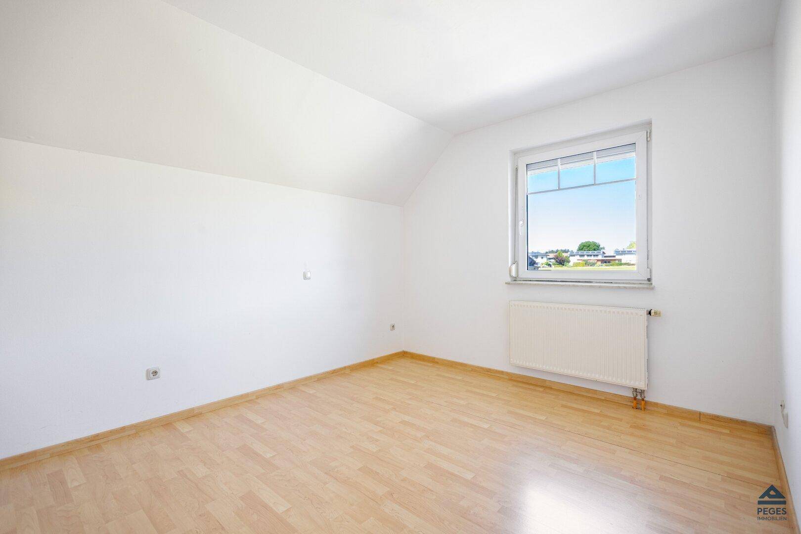 Helles Schlafzimmer mit Holzboden, weißen Wänden und Dachschräge.