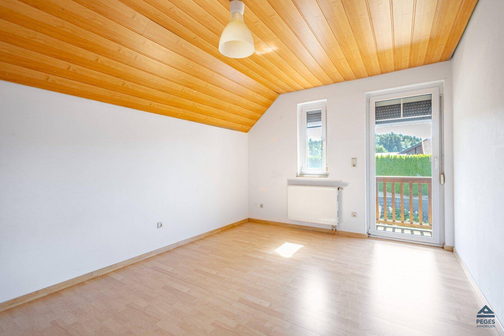 Heller Raum mit Holzboden, Holzdecke und Zugang zu einem kleinen Balkon.
