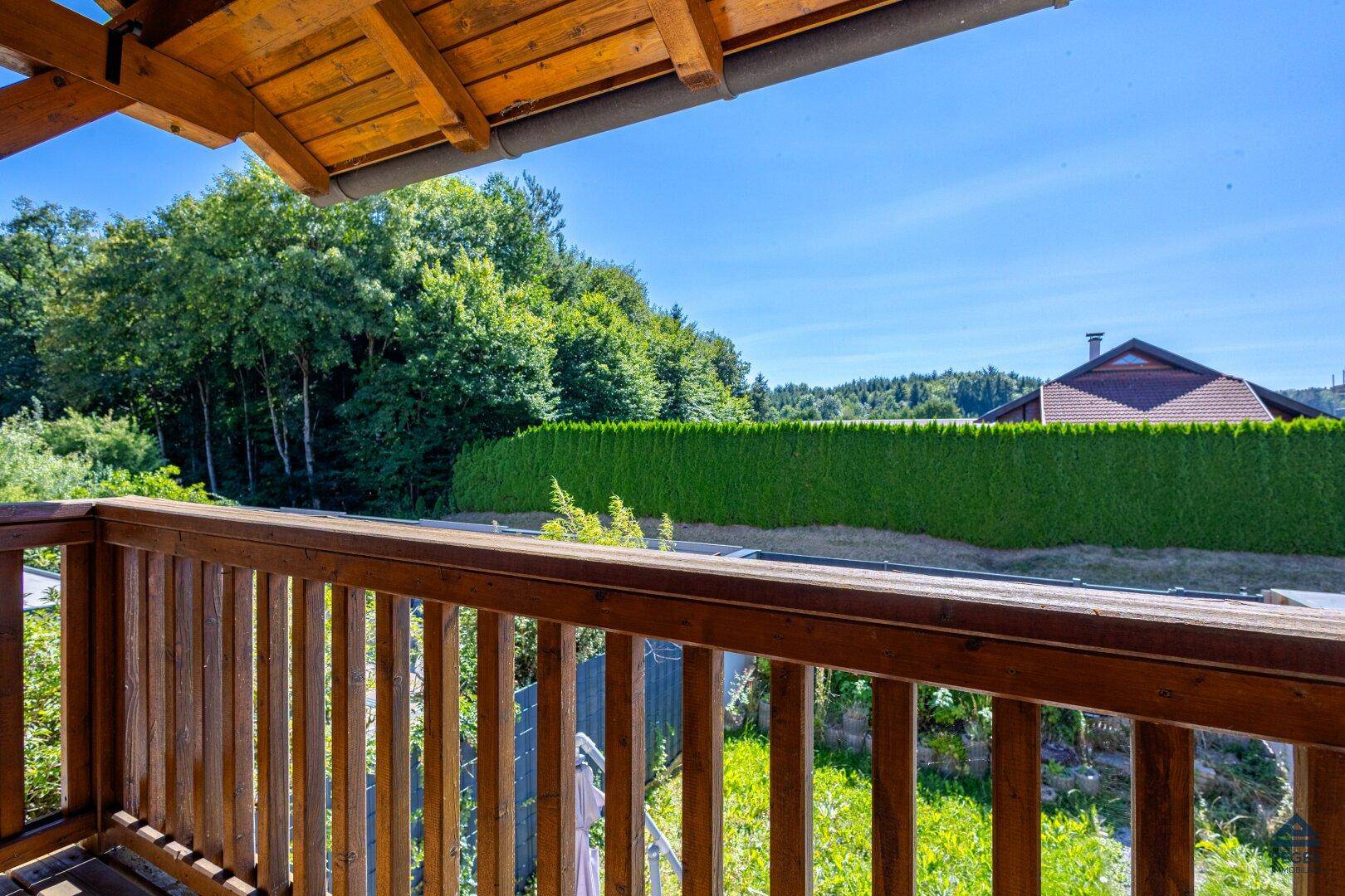Blick vom Holzbalkon ins Grüne mit weitreichender Aussicht und blauem Himmel.