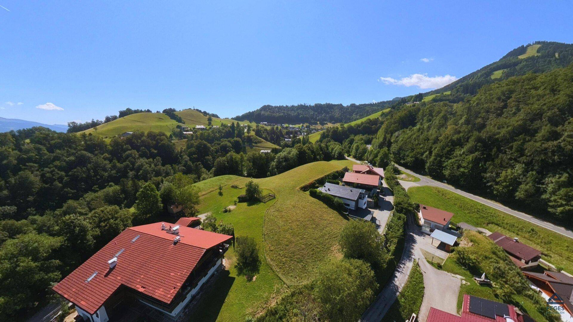 Weitwinkel-Luftaufnahme einer Wohnsiedlung, eingebettet in eine malerische grüne Landschaft mit bewaldeten Hügeln.