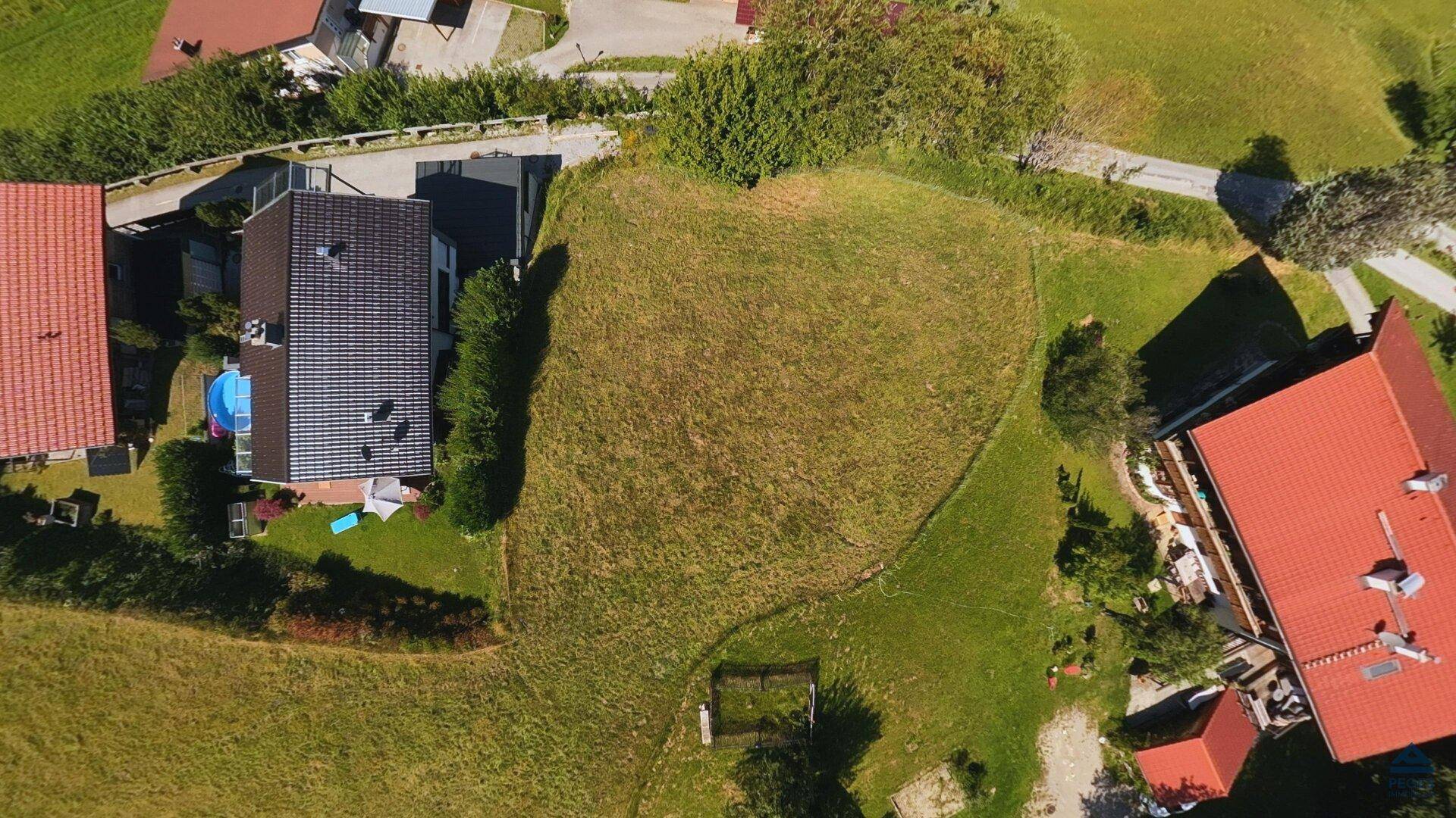 Luftaufnahme eines großen, unbebauten Grundstücks, umgeben von Wohnhäusern und einer Straße in ländlicher Umgebung.