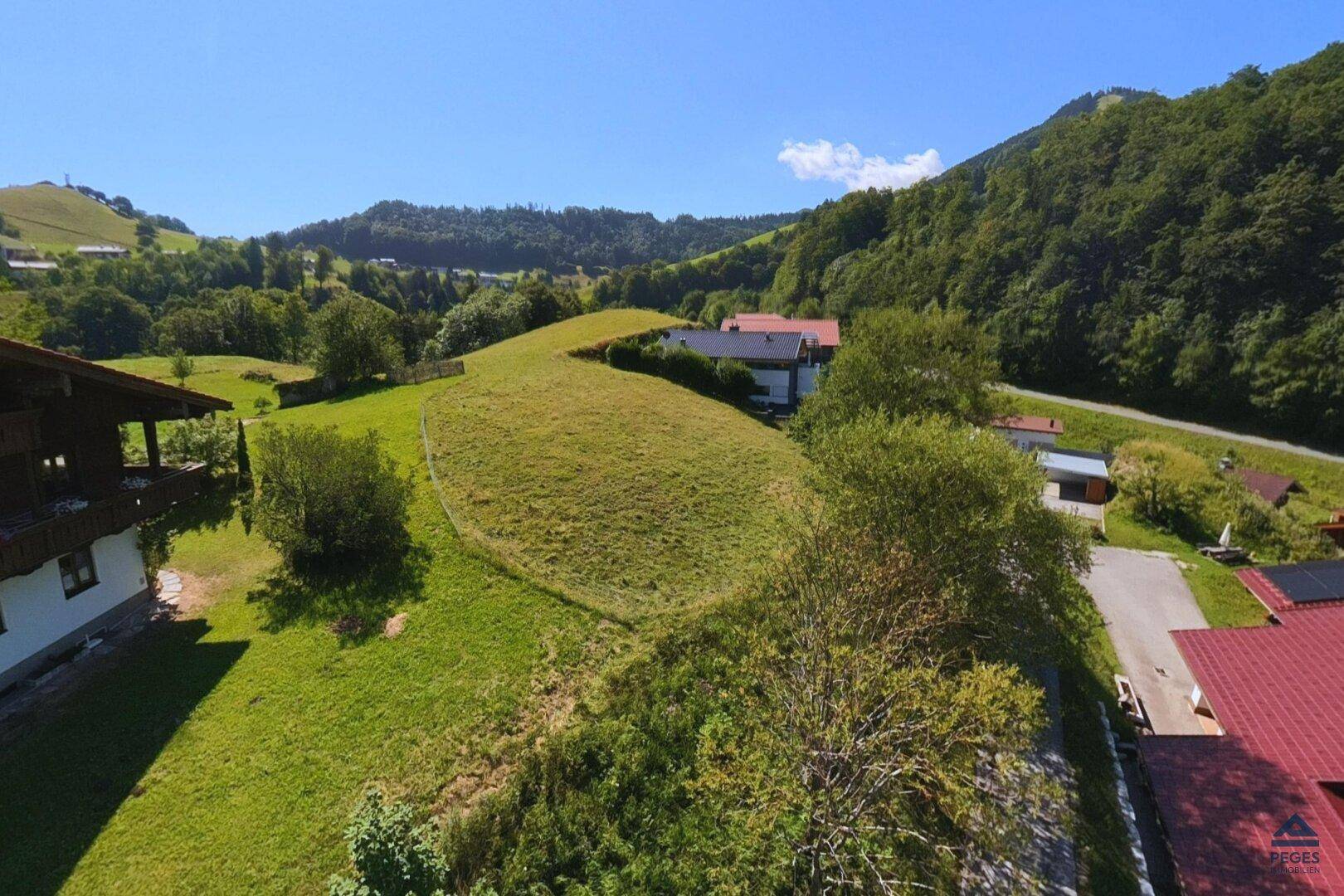Idyllischer Ausblick auf sanfte grüne Hügel und vereinzelte Häuser unter einem strahlend blauen Himmel.