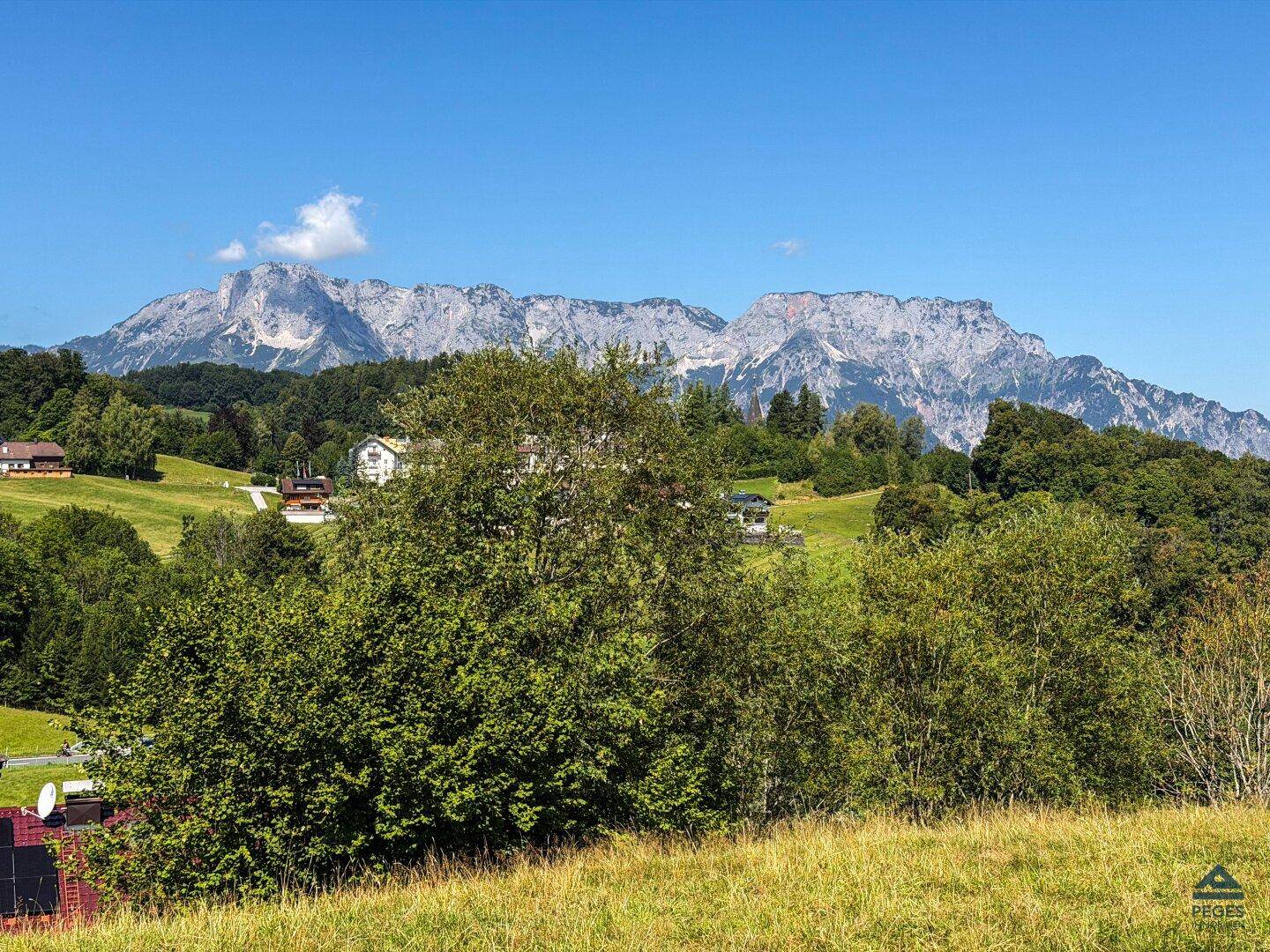 Weitläufiger Blick über eine grüne Landschaft mit üppiger Vegetation und einer beeindruckenden Bergkette am Horizont.