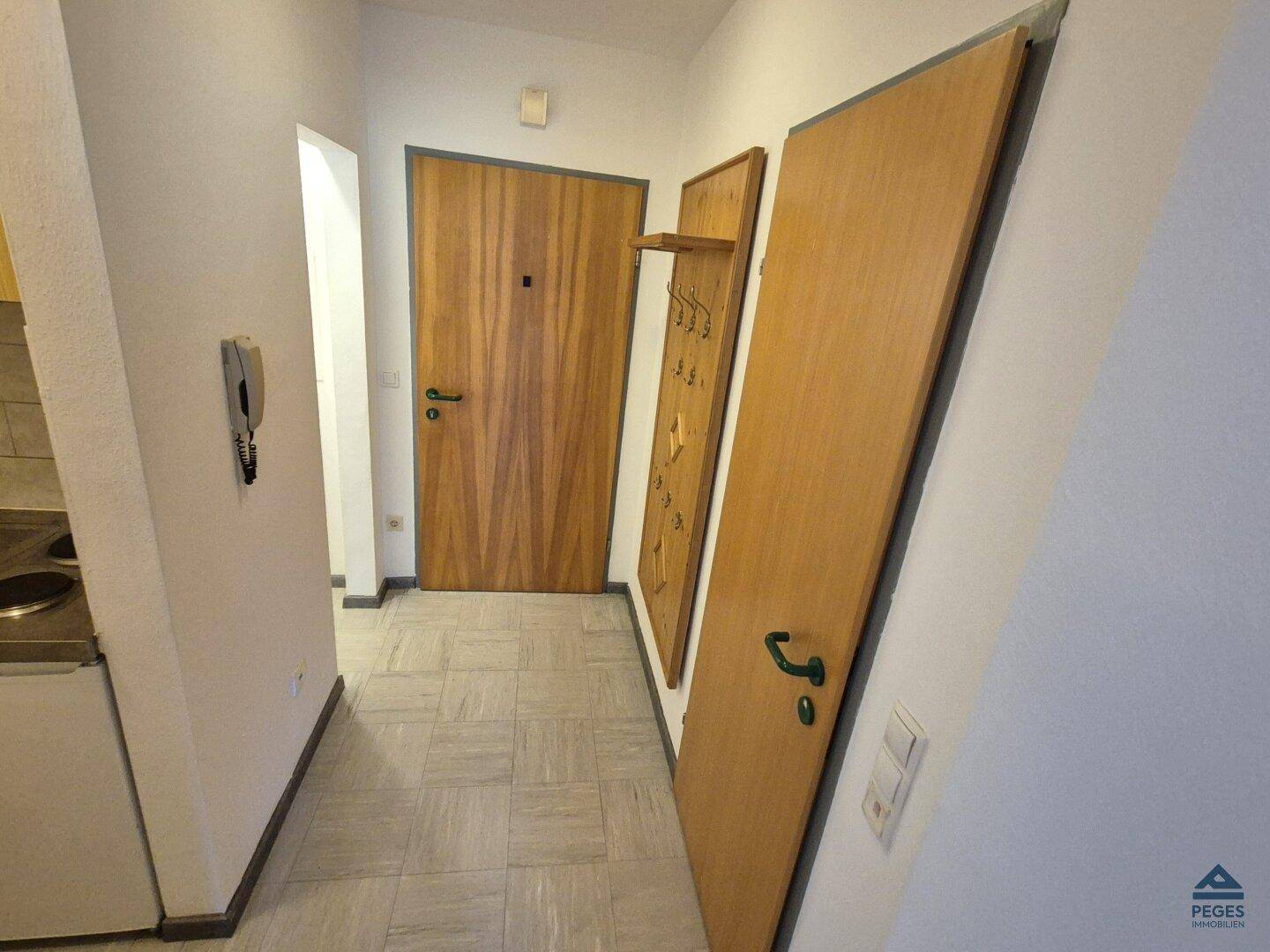 Heller Flur mit Holztüren, Fliesenboden und einer Garderobe im Eingangsbereich.