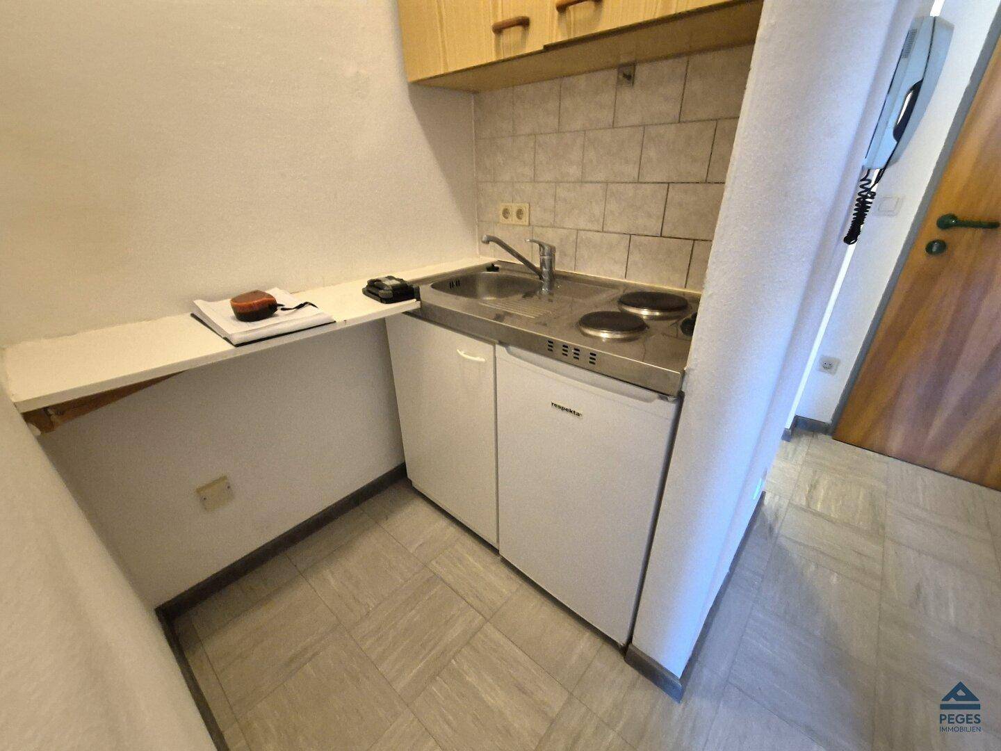 Kompakte Küchenzeile mit Spüle, zwei Kochplatten und einem kleinen Kühlschrank.