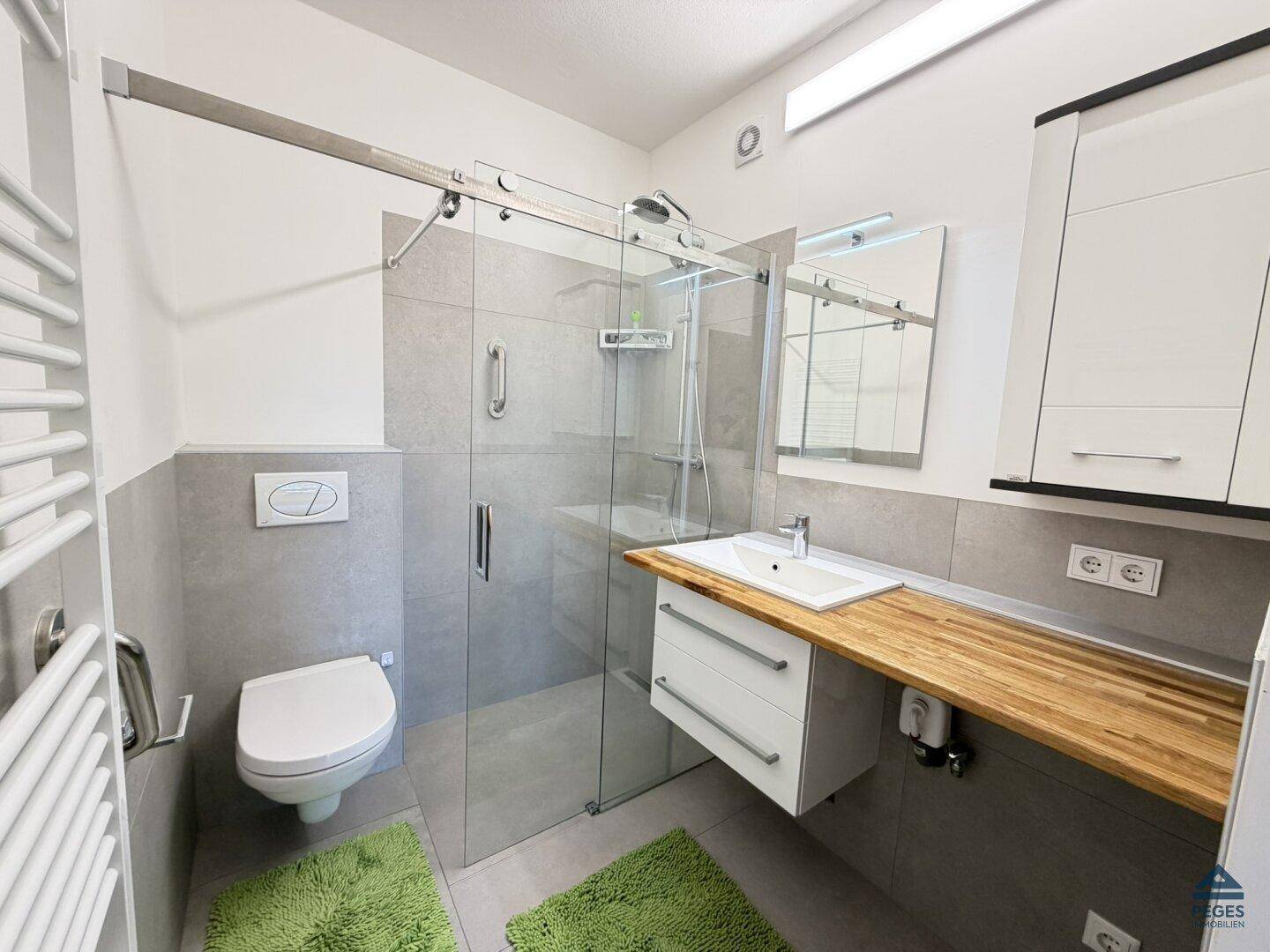 Modernes Badezimmer mit begehbarer Dusche, Wand-WC, Holzwaschtisch und Handtuchheizkörper.