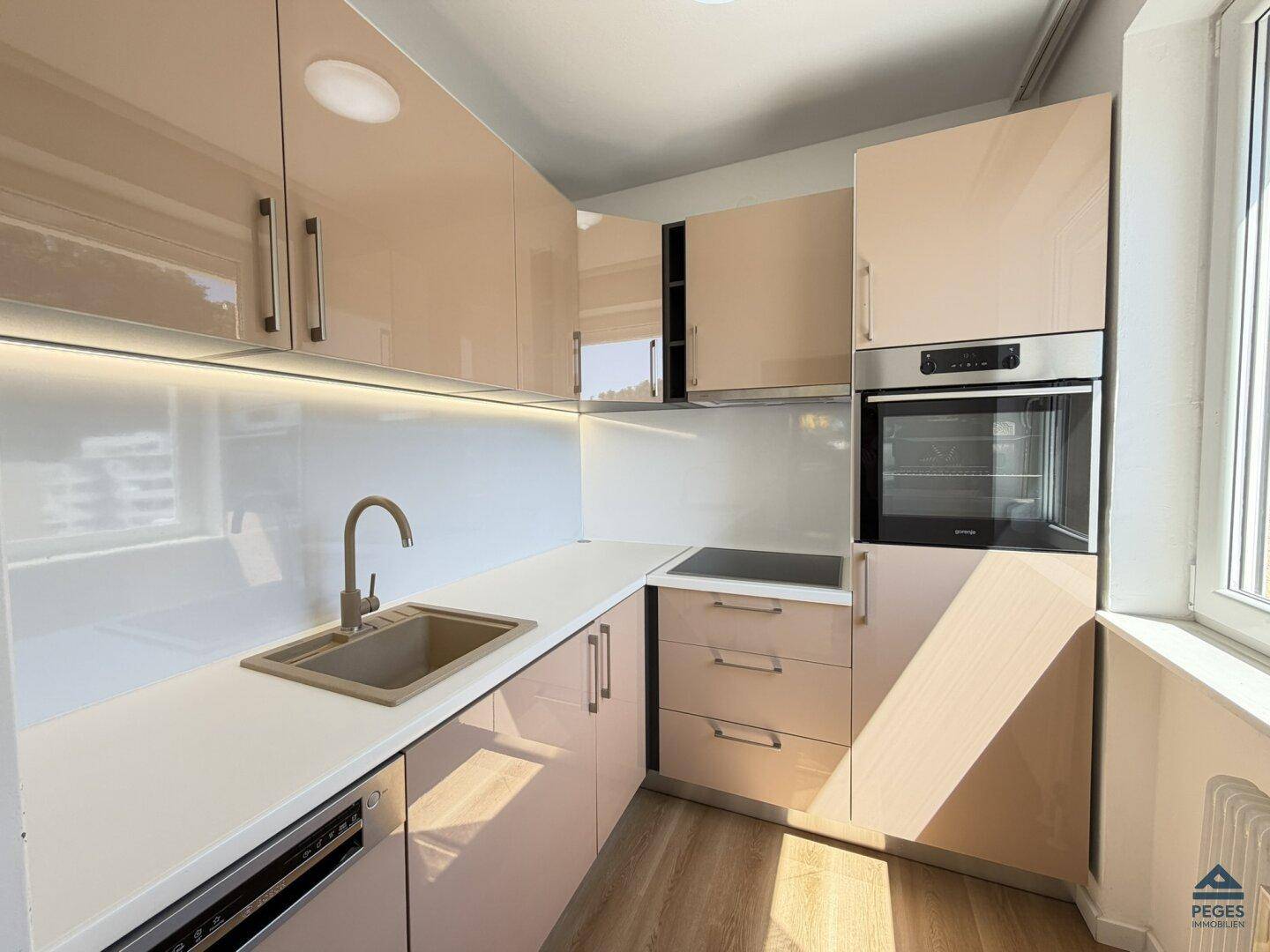 Moderne Küche mit beigen Hochglanzfronten, Einbaugeräten und Fenster für Tageslicht.