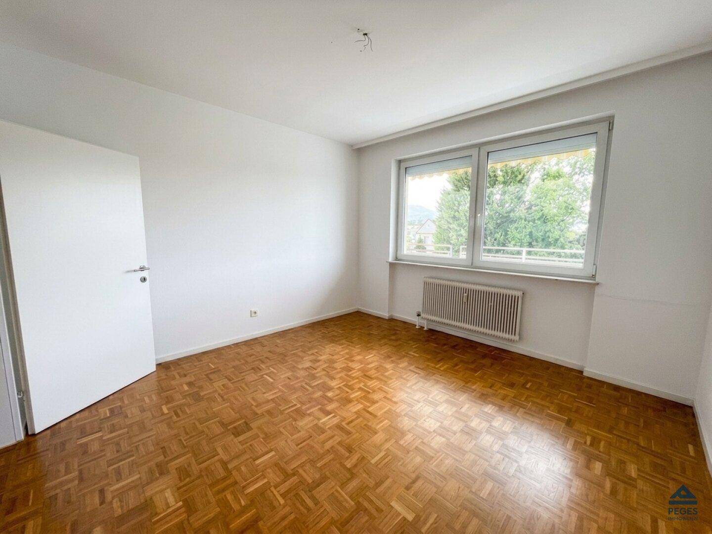 Geräumiges Schlafzimmer mit Parkettboden, großen Fenstern und viel Tageslicht.