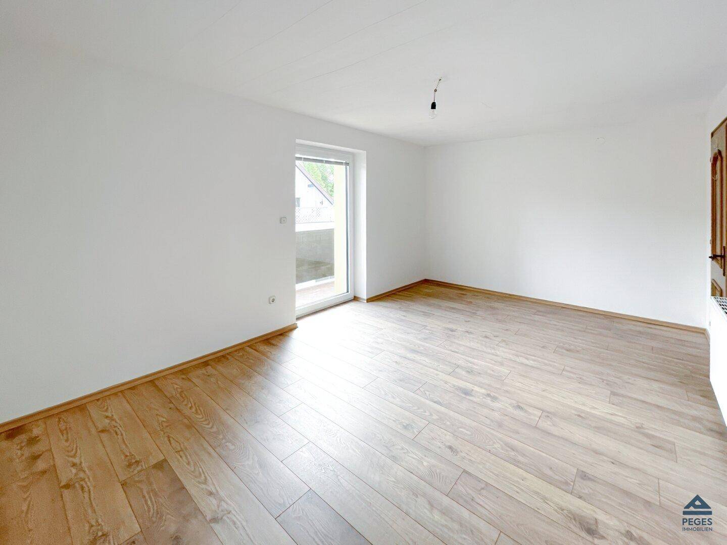 Geräumiger, heller Raum mit Holzboden und direktem Zugang zu einem Balkon, ideal für frische Luft.
