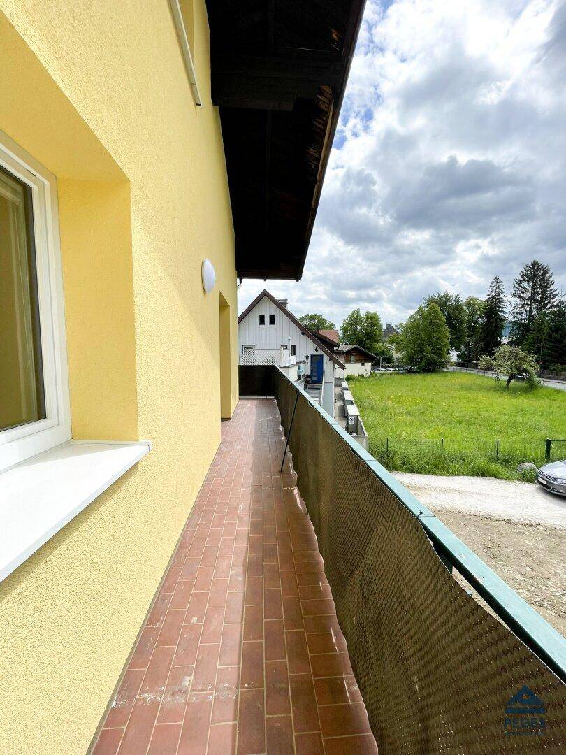 Langer Balkon mit Terrakottafliesen und Blick auf eine grüne Wiese und die umliegende Landschaft.