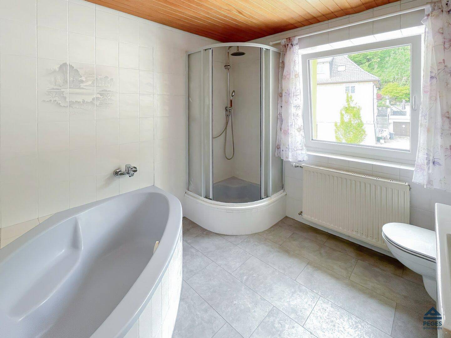 Helles Badezimmer mit Badewanne, Eckdusche, WC und einem Fenster für natürliche Belüftung.