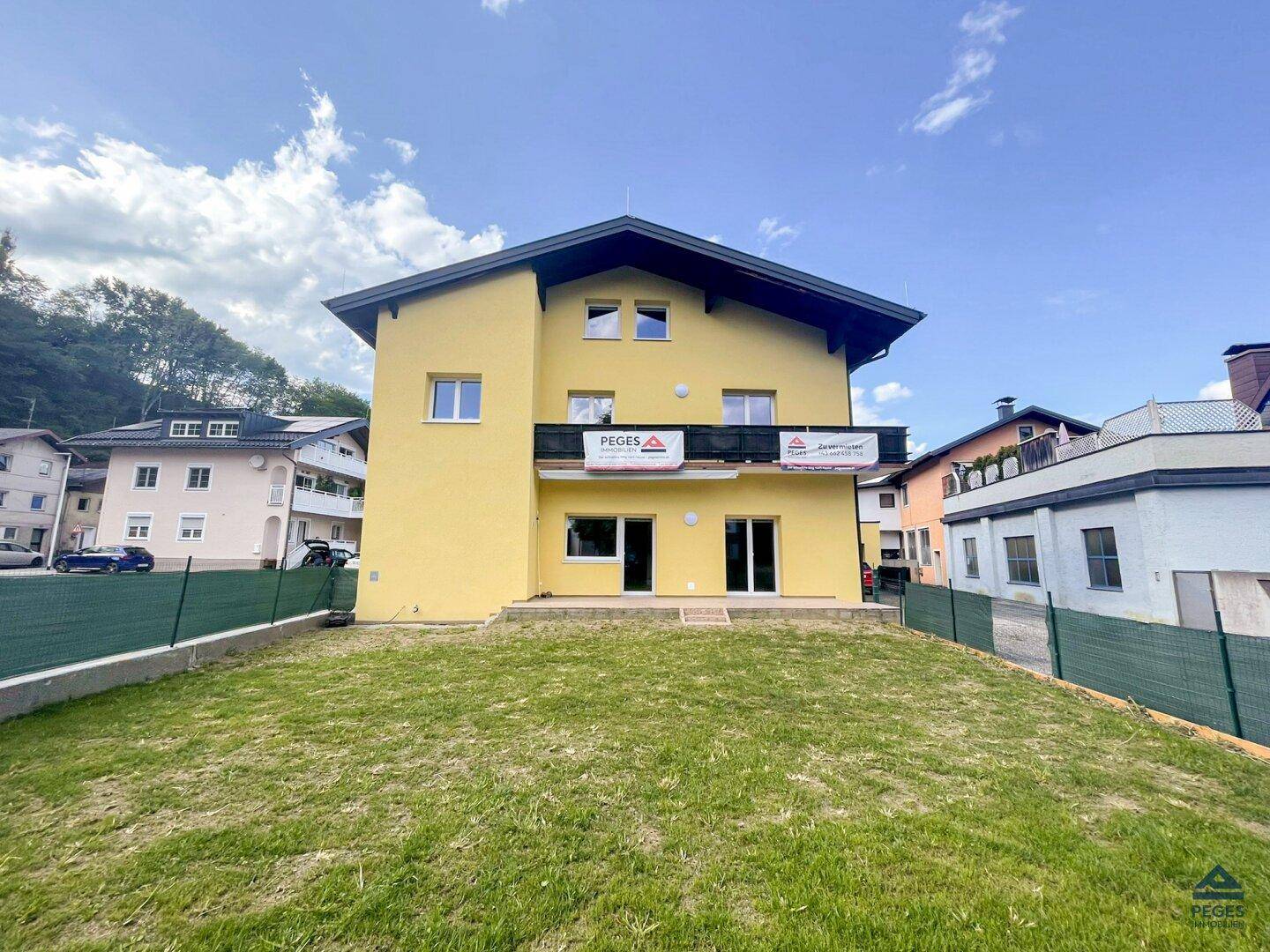 Gelbes Wohnhaus mit Balkon und großem Gartenbereich, umgeben von grünen Hügeln.