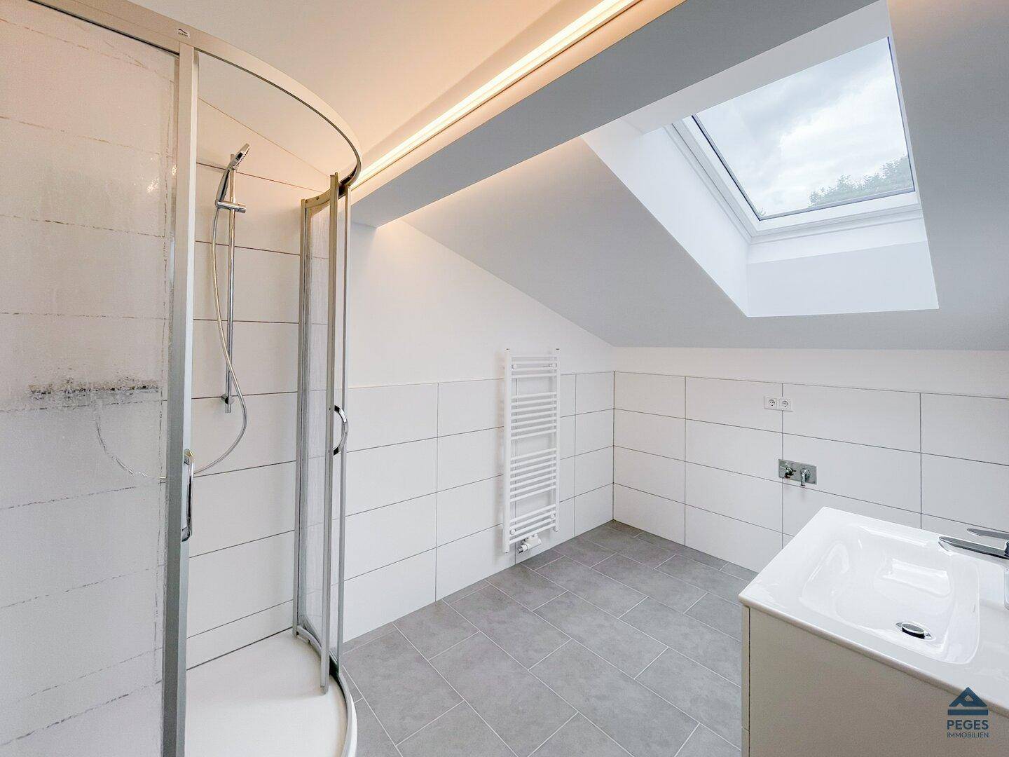 Modernes Badezimmer mit Duschkabine, Dachfenster, beheiztem Handtuchhalter und hellen Fliesen.