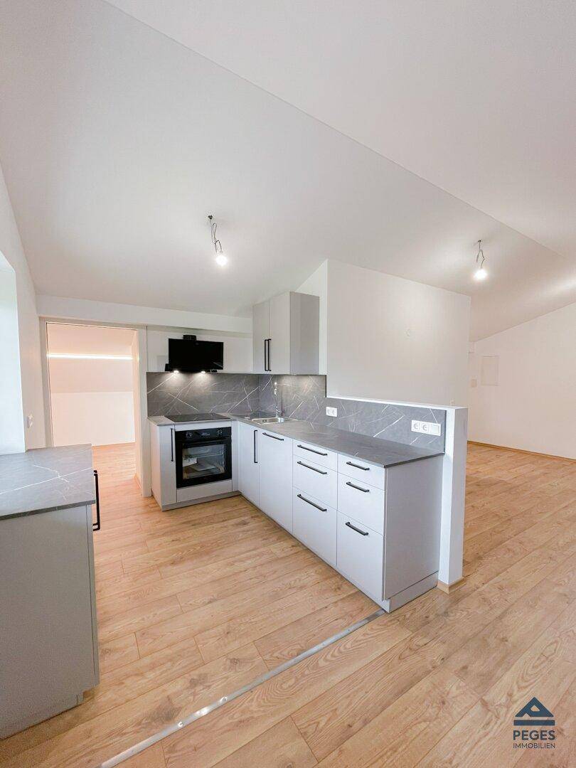 Moderne, unmöblierte Küche mit grauen Schränken, integriertem Backofen und Holzboden.