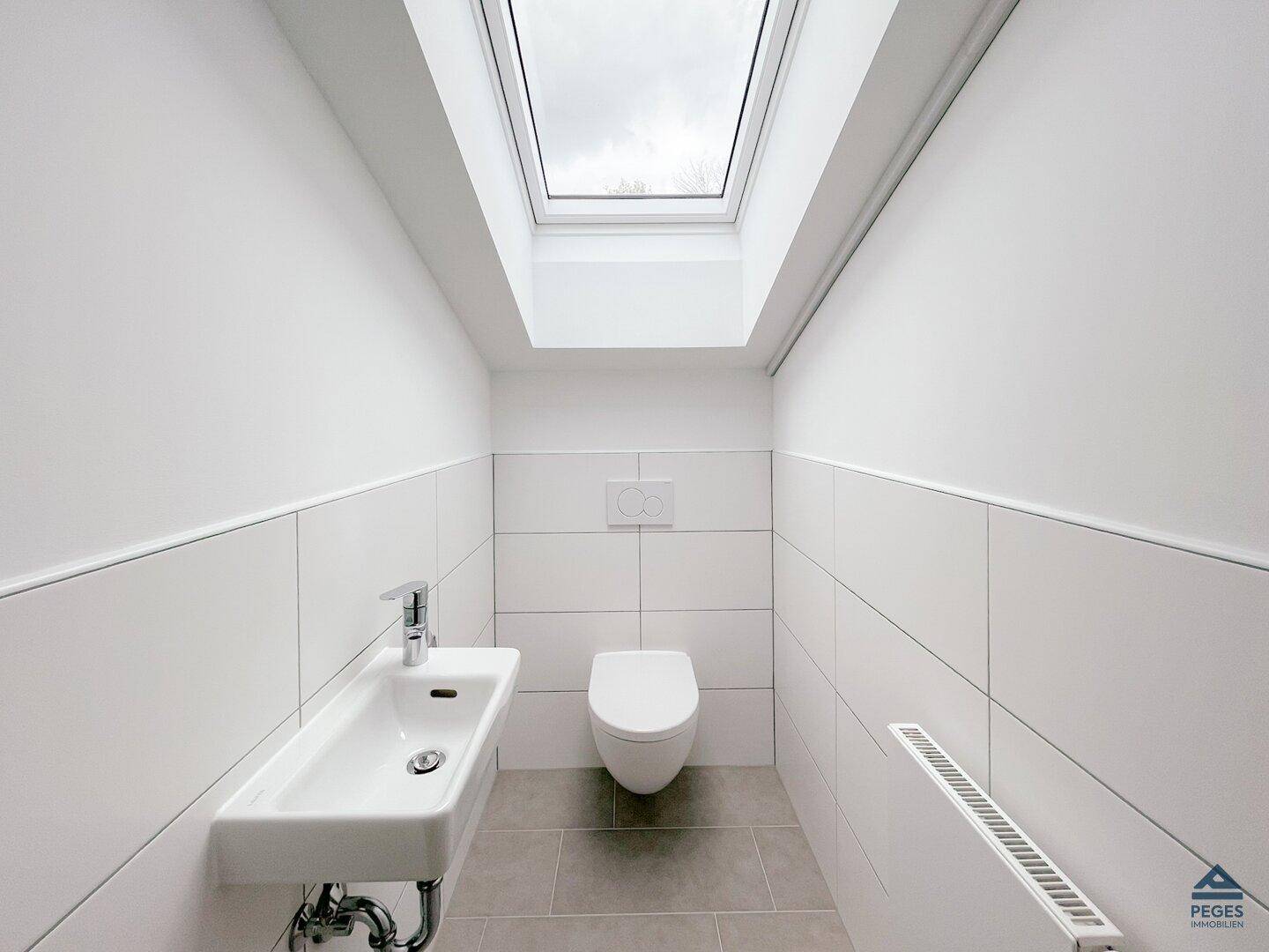Kleines Gäste-WC mit modernem Waschbecken, Toilette und einem Dachfenster für Tageslicht.