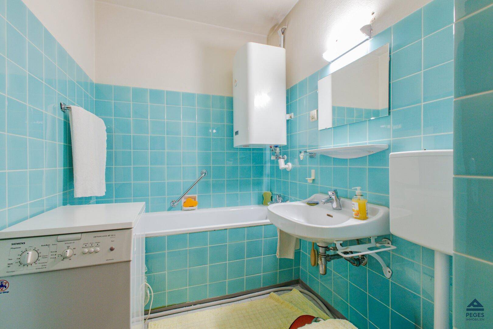 Badezimmer mit türkisfarbenen Fliesen, Badewanne, Waschbecken und einer Waschmaschine.
