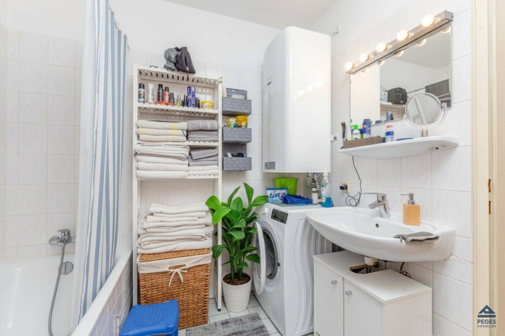Praktisches Badezimmer mit Badewanne, Waschbecken, Waschmaschine und Stauraumregalen.