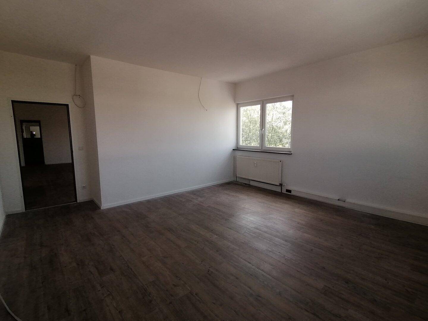 Heller Raum mit Holzoptik-Boden und einem Fenster, das Tageslicht hereinlässt.