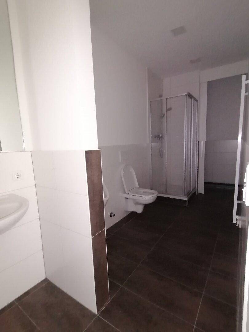 Modernes Badezimmer mit Duschkabine, Toilette, Waschbecken und braunen Fliesen.