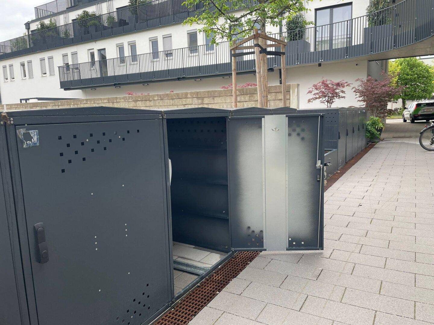 Moderne Fahrradboxen vor einem Wohngebäude mit Balkonen.