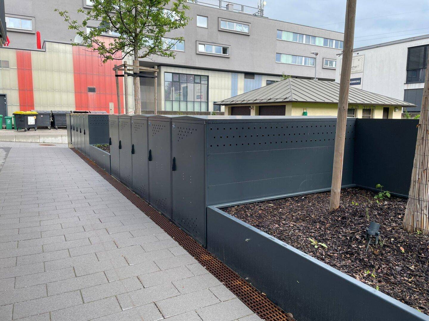Reihe von modernen Fahrradboxen entlang eines gepflasterten Weges.