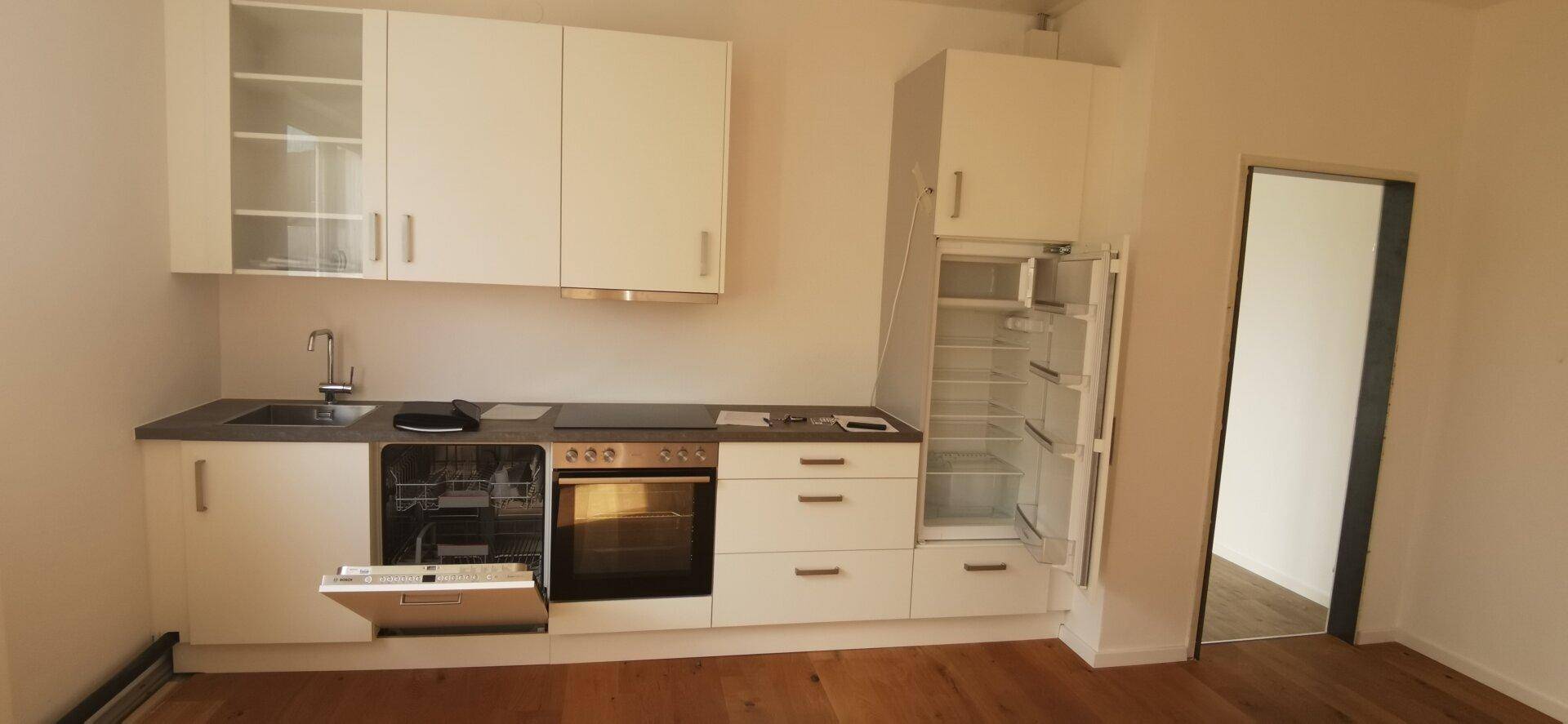 Moderne Einbauküche mit weißen Schränken, integrierten Geräten und Holzboden.