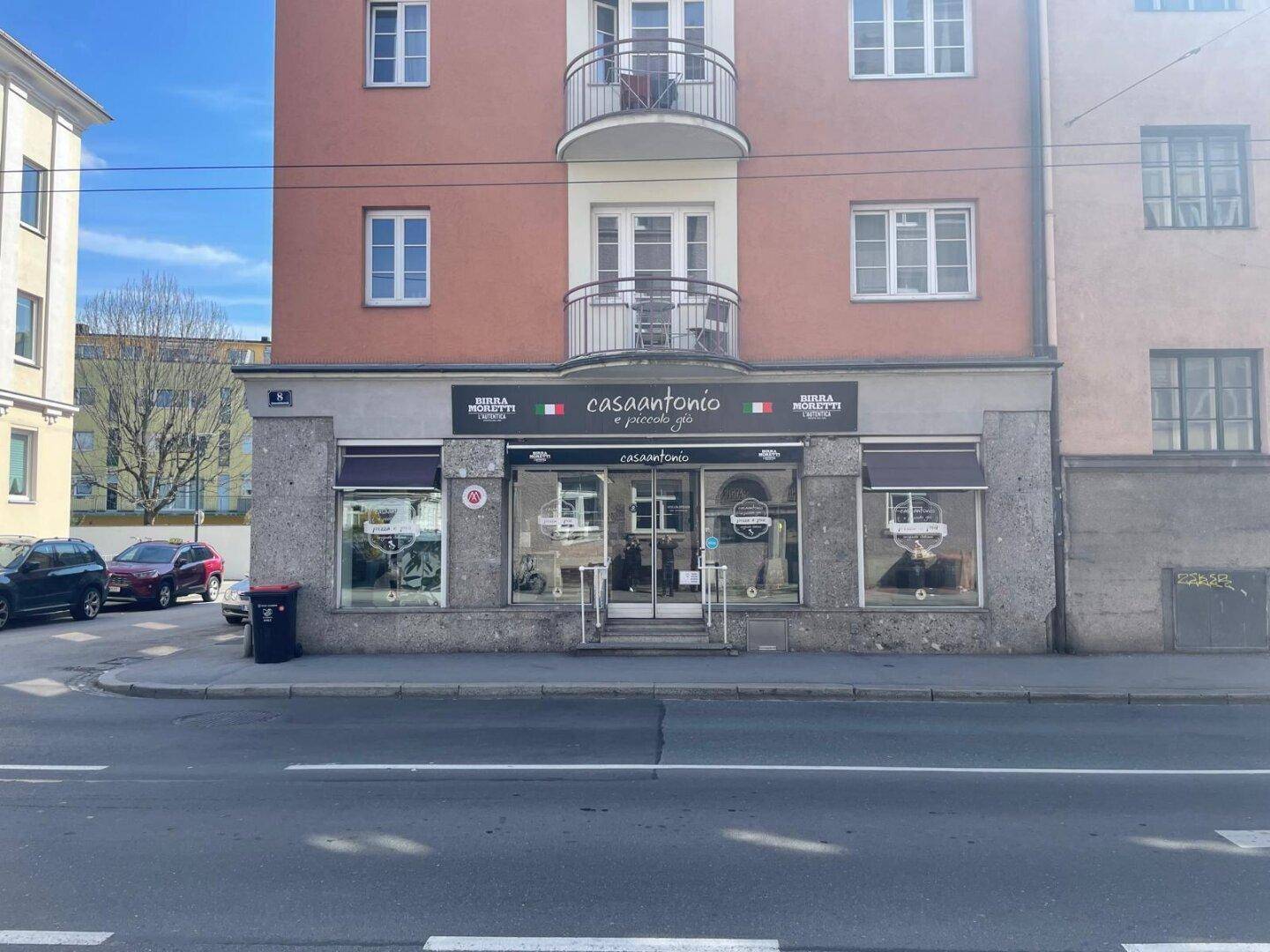 Fassade eines Geschäftsgebäudes mit Restaurant im Erdgeschoss und Wohnungen darüber, direkt an einer Straße gelegen.