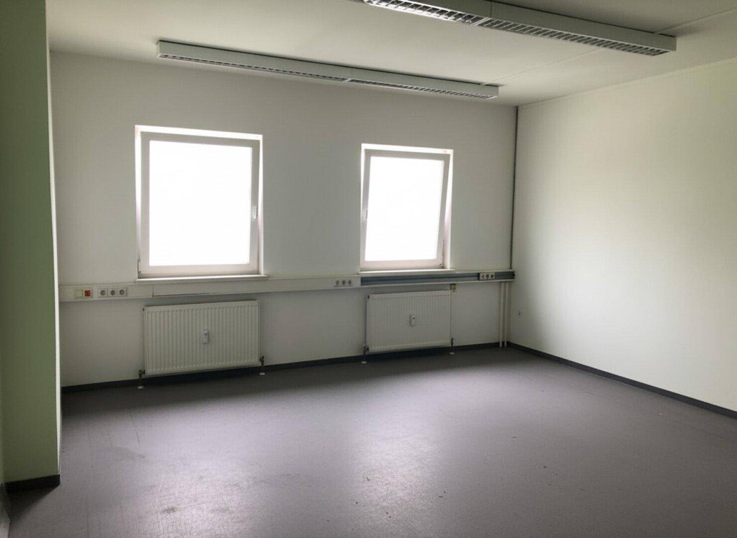 Helles Büro mit strapazierfähigem Bodenbelag, zwei Fenstern und funktionaler Deckenbeleuchtung.